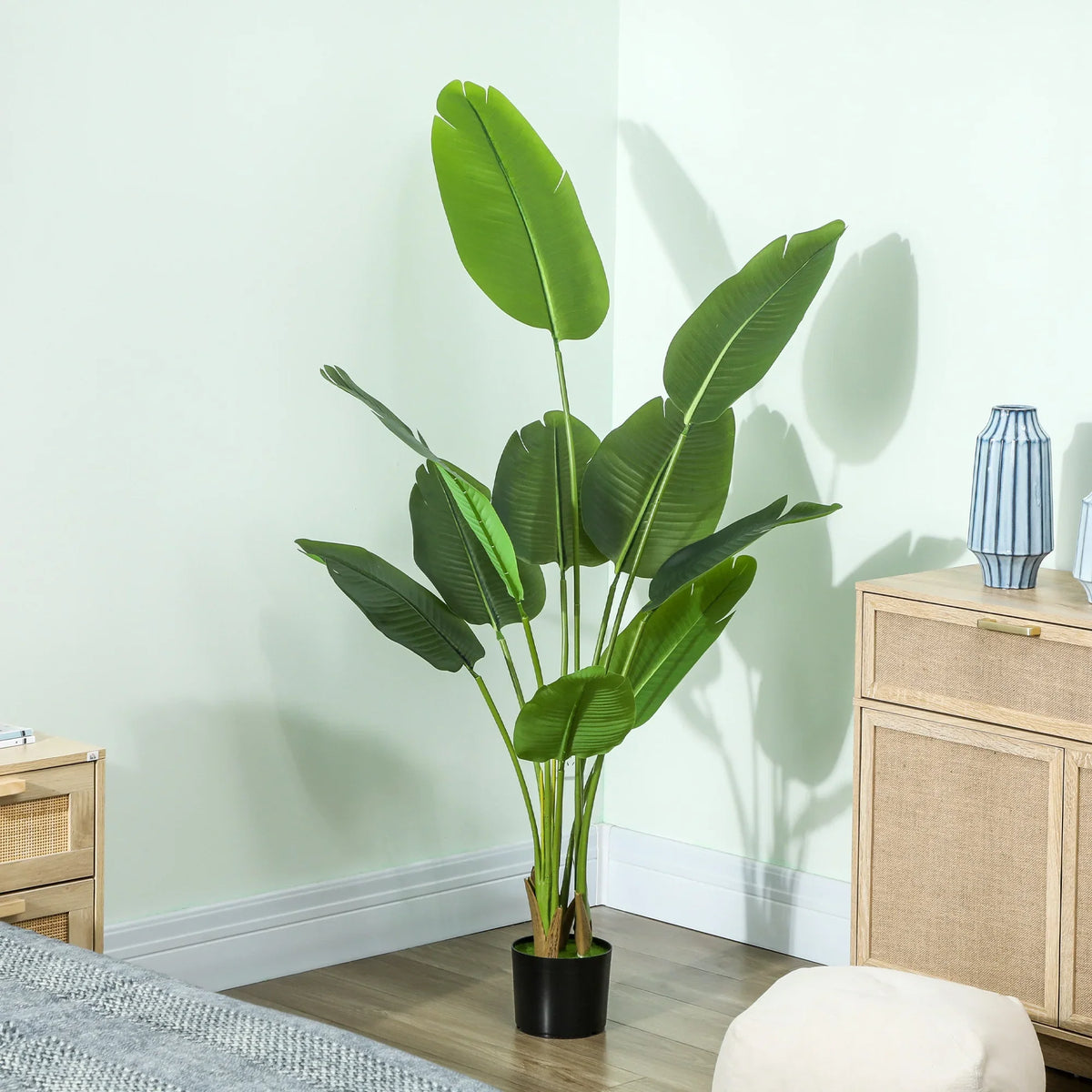 Artificial bird of paradise plant with green leaves in black pot against white wall