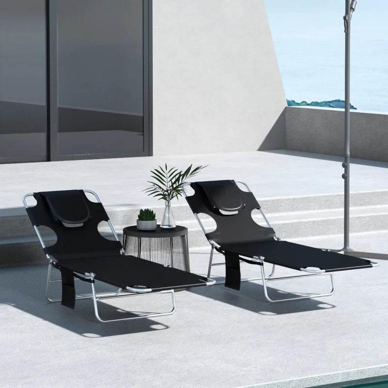 Pair of black foldable sun loungers with adjustable backrests and face cutout pillows