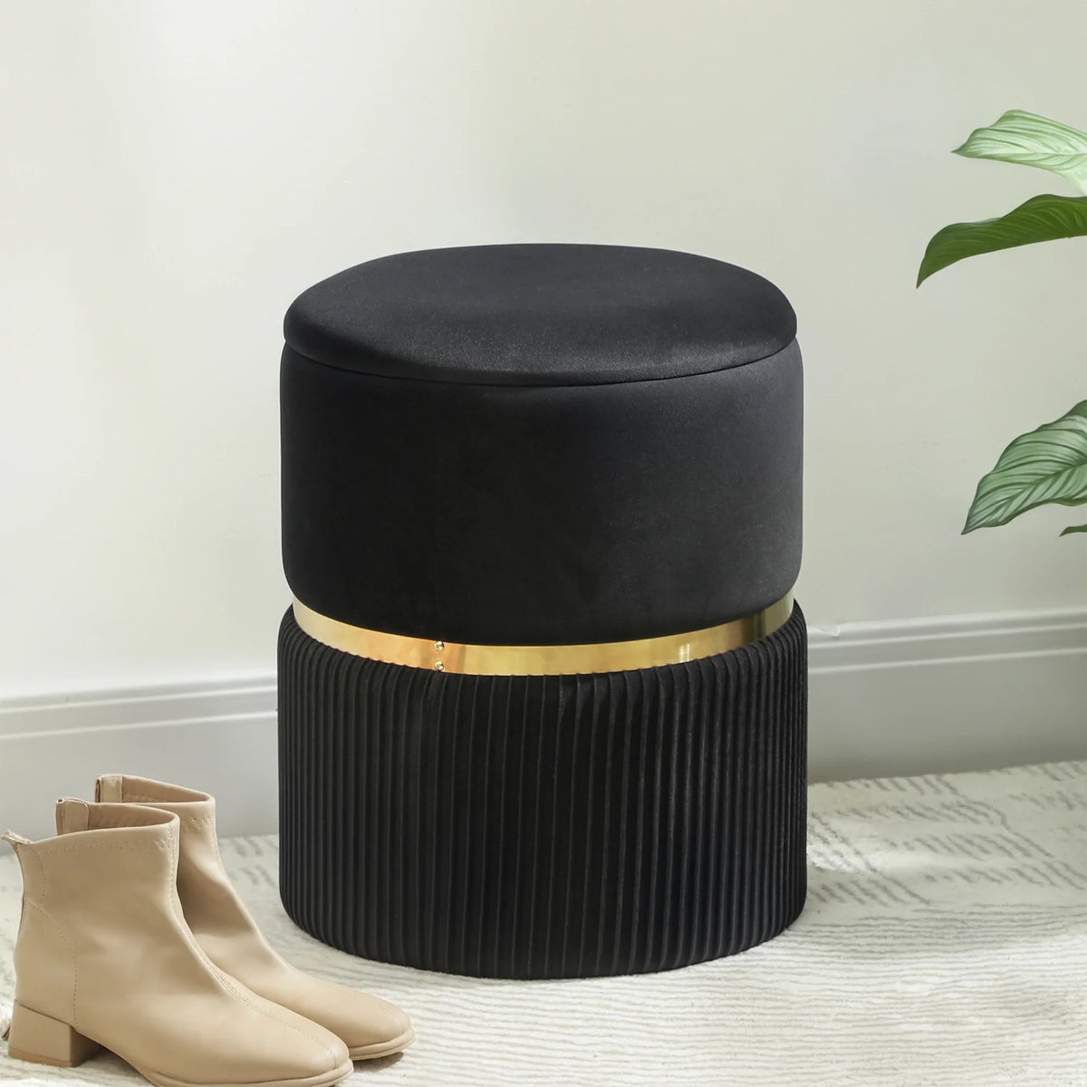Black round storage ottoman with velvet-look top, ribbed sides, and gold-tone band