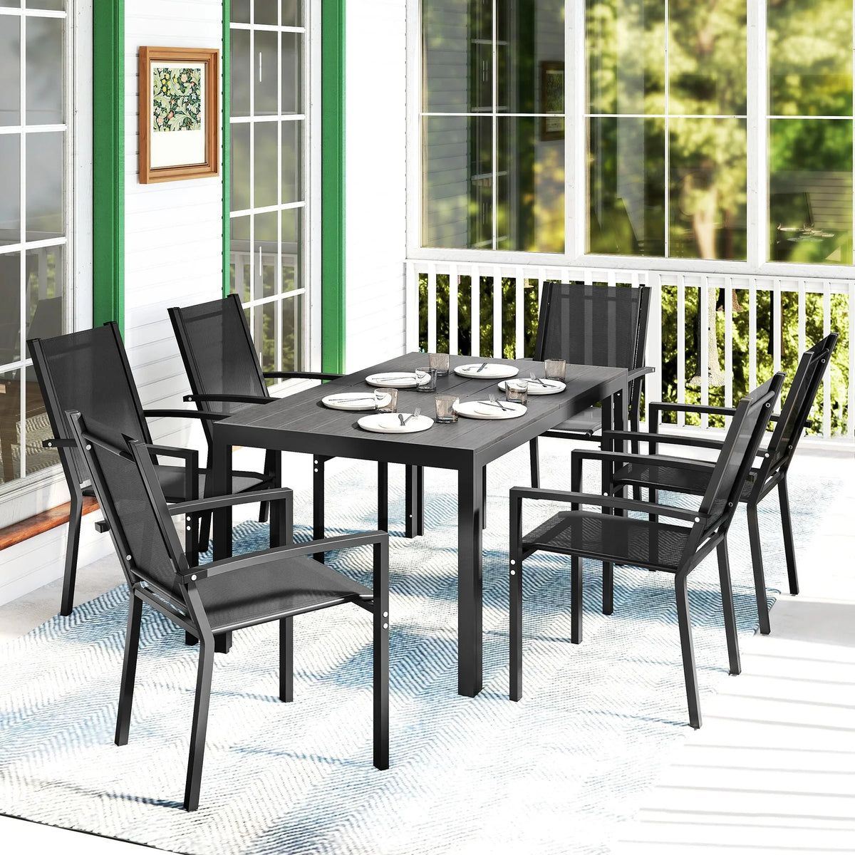 Black outdoor dining table with stackable mesh chairs on patio near railing