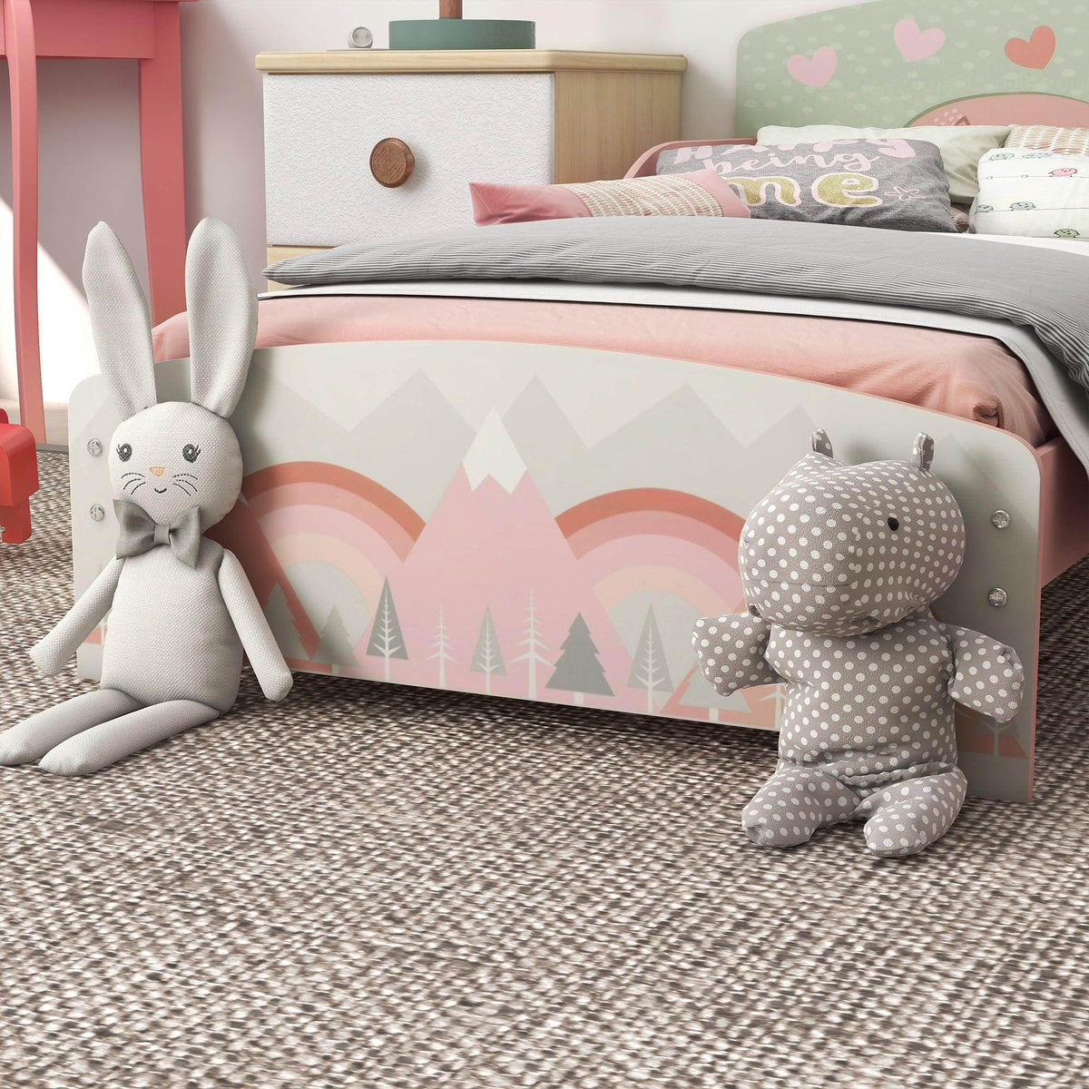 Pink toddler bed with rainbow mountain panel, rounded headboard, and plush bunny toys
