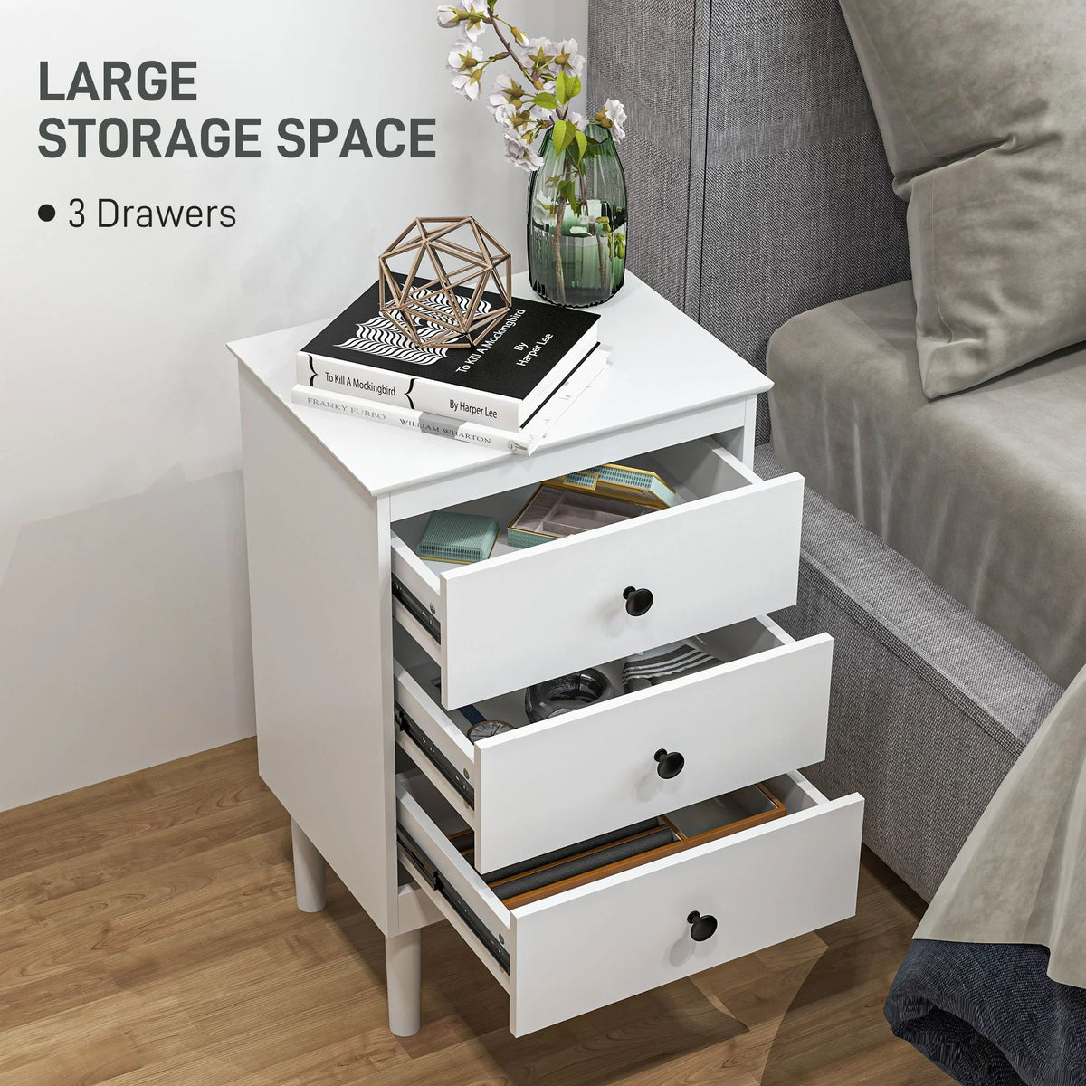 White bedside table with three drawers, featuring open storage sections and black knobs