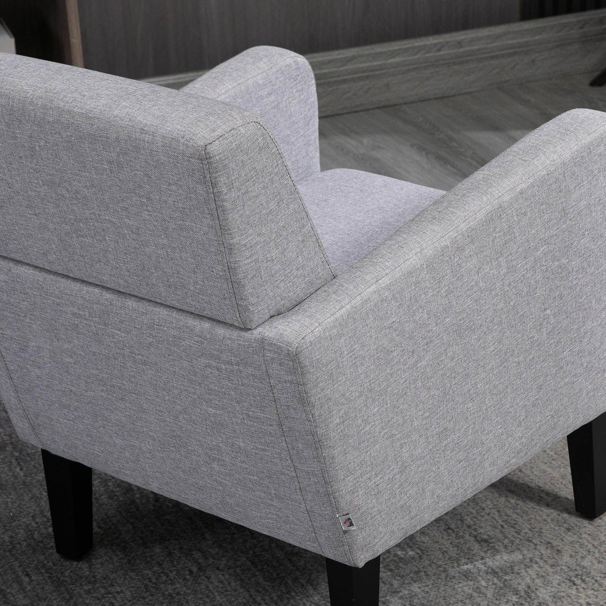 Light grey upholstered armchair with stitched seams and black wooden legs