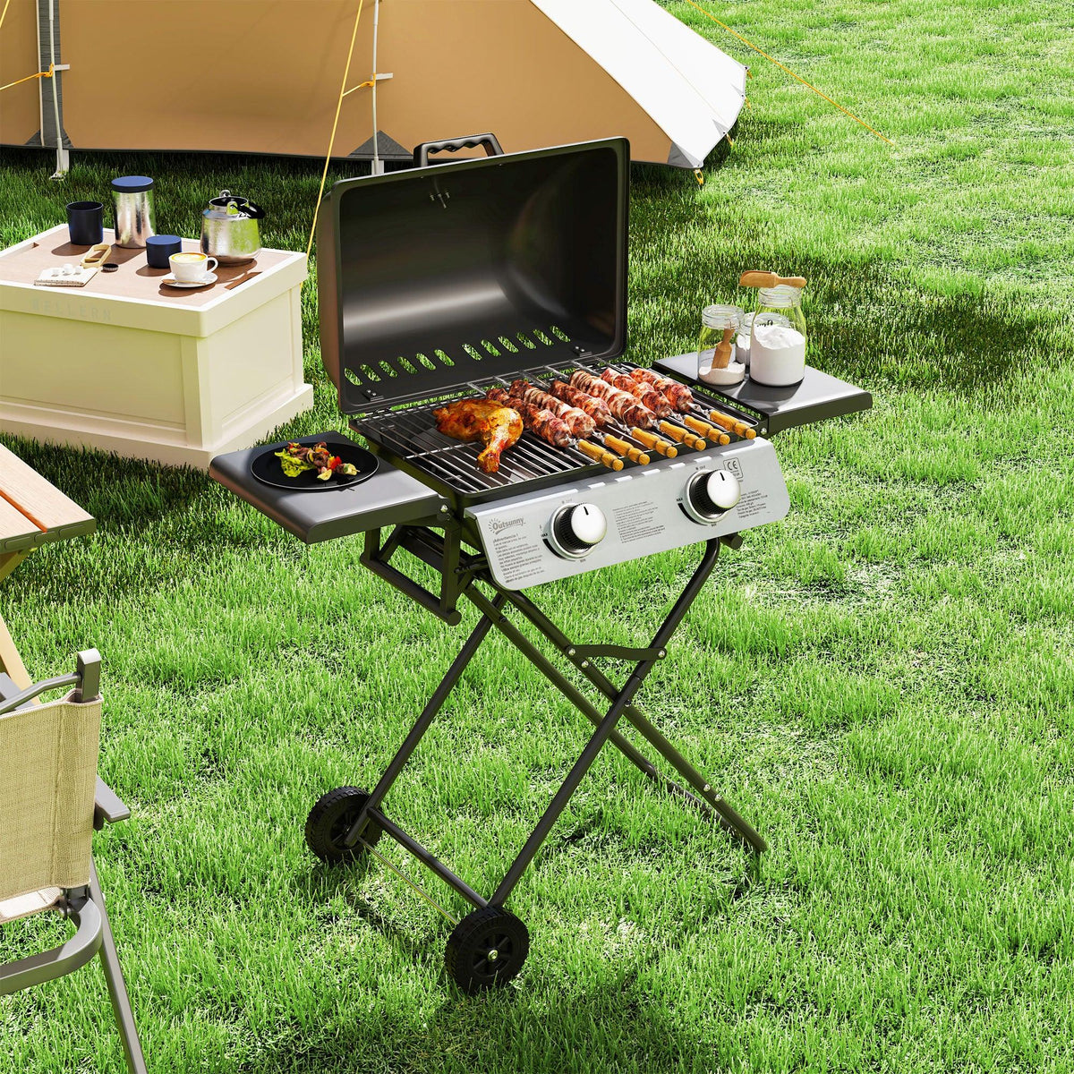 Black two-burner portable gas grill on folding stand with side tables and cooking food