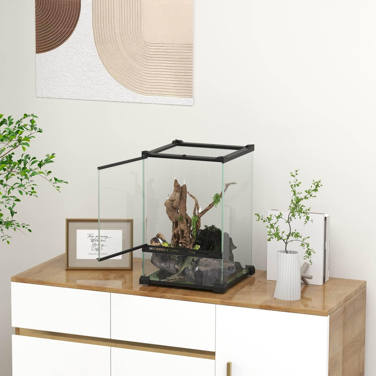 Glass reptile terrarium with black frame on a wooden cabinet, with branches inside
