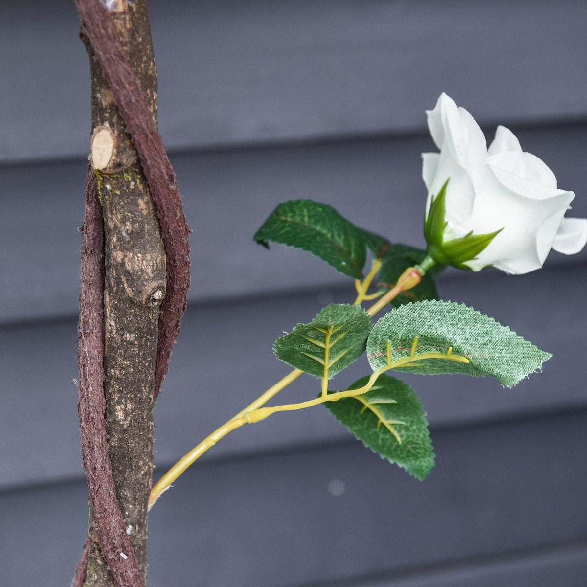 Close-up of an artificial white rose bloom with green leaves on a brown stem