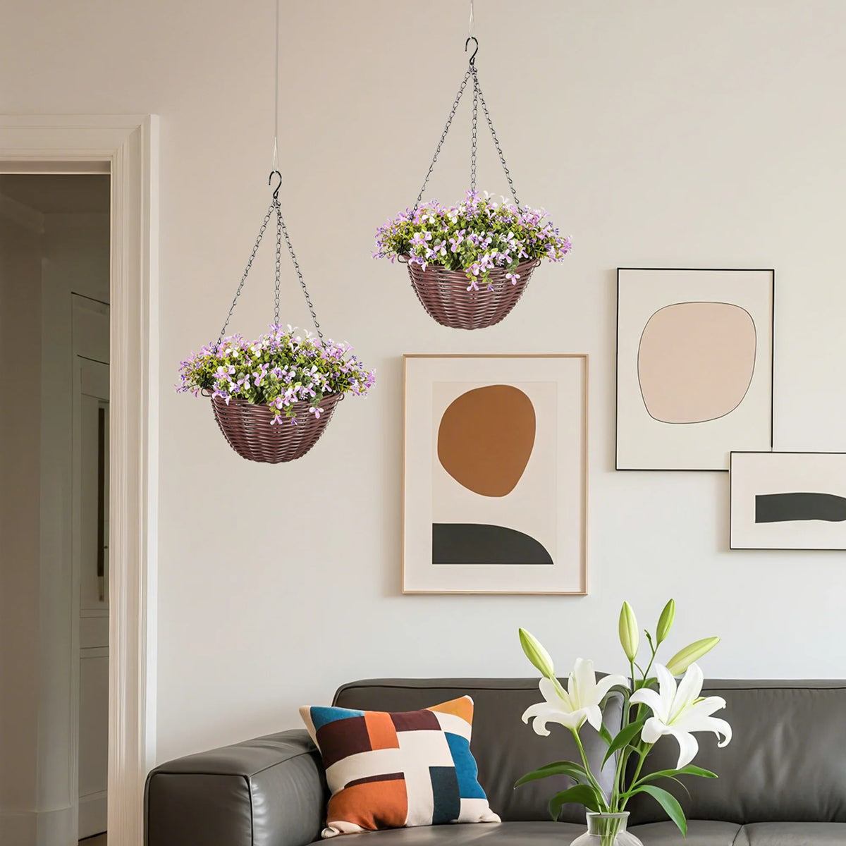 Set of 2 hanging baskets with purple faux flowers and green leaves above a living room couch