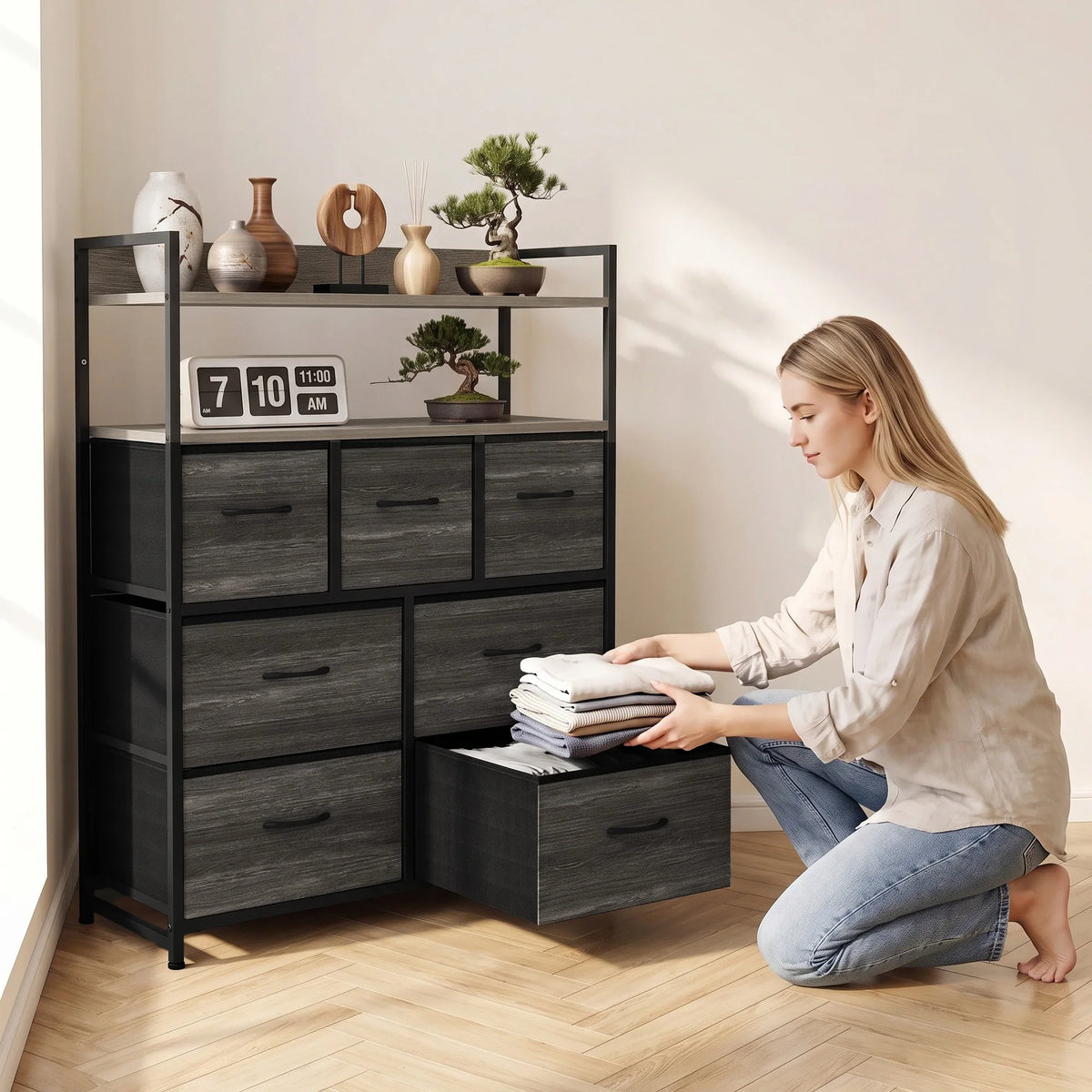 Grey wood-effect dresser with open shelves and seven drawers; person arranging folded items