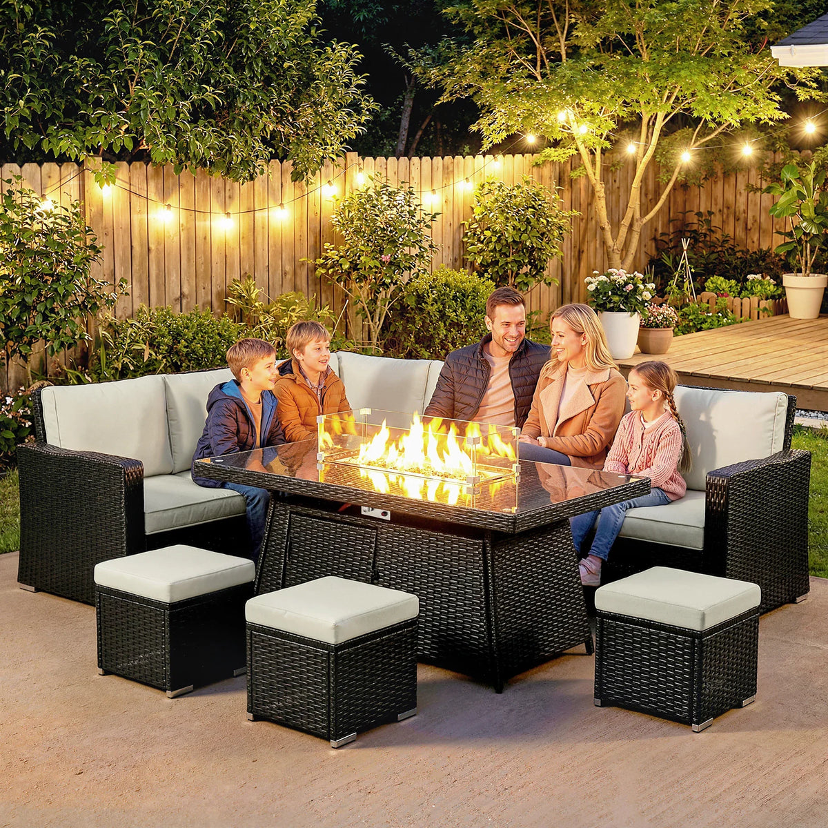 Outdoor corner sofa set with black rattan frame, beige cushions, and lit fire pit table.