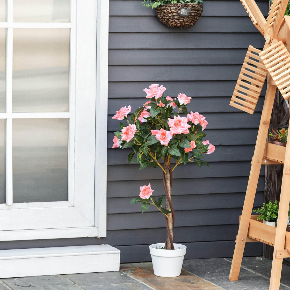 Artificial pink rose plant in a white pot on outdoor steps by a gray house wall