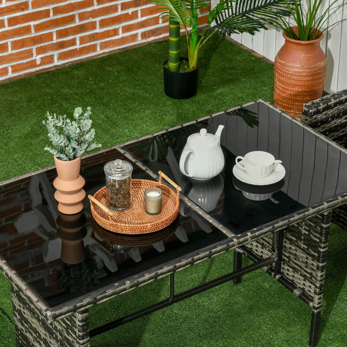 Glass-top coffee table with dark gray rattan frame and tabletop items on patio