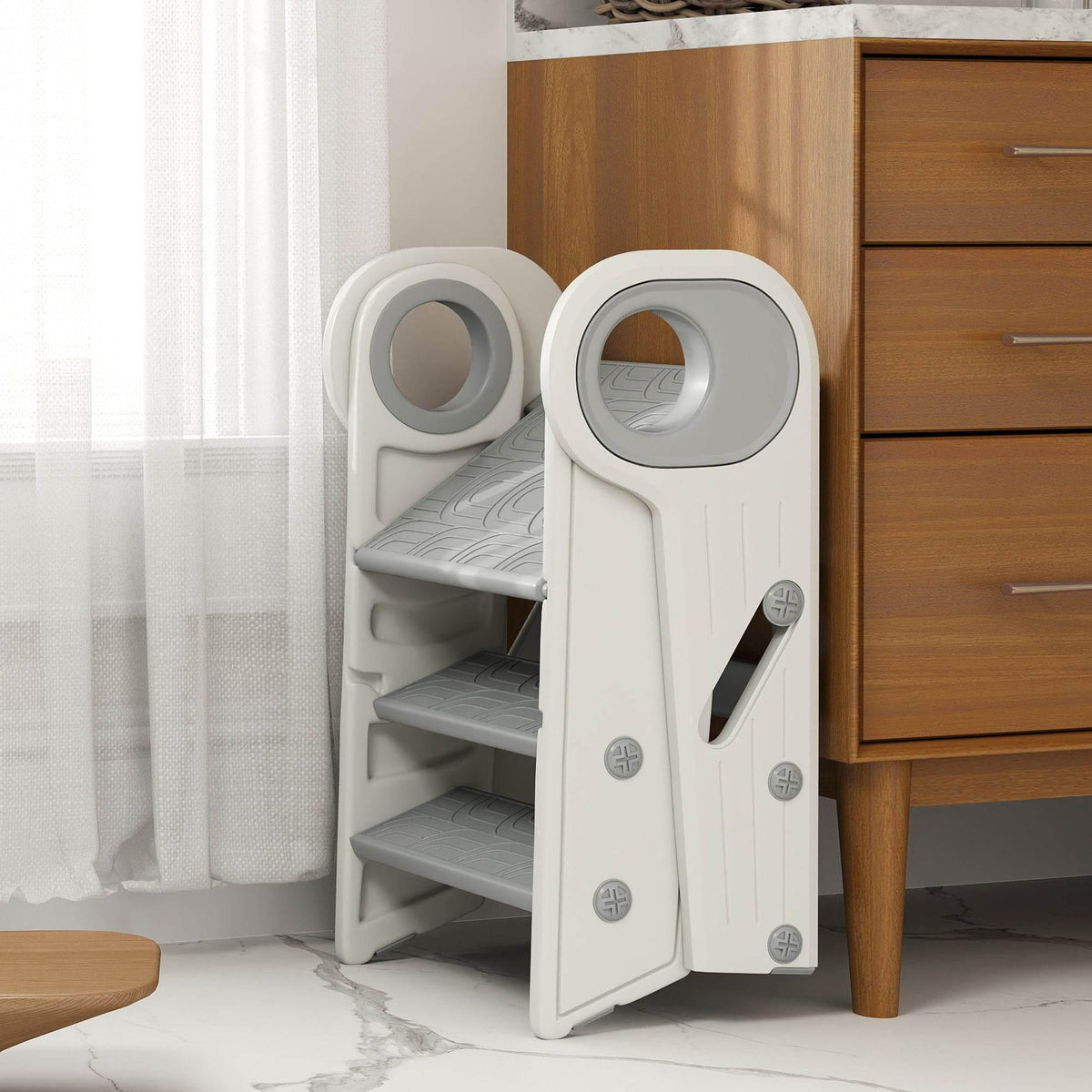 Toddler step stool with light gray steps and circular openings, positioned near a cabinet.