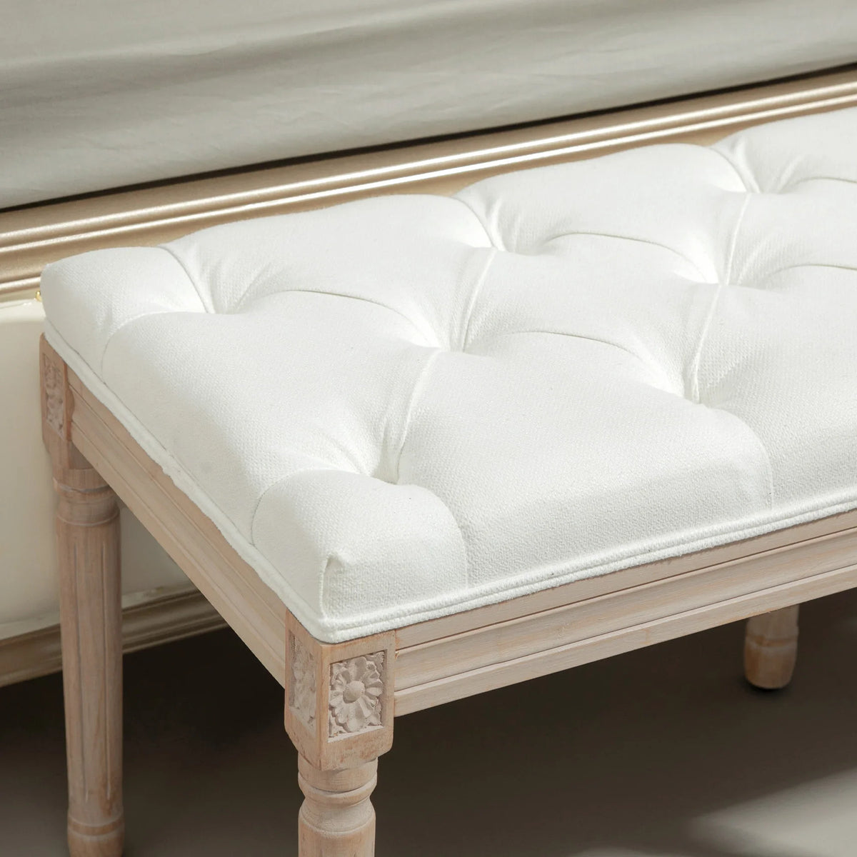 Cream tufted padded bench with light wood frame and carved corner panel