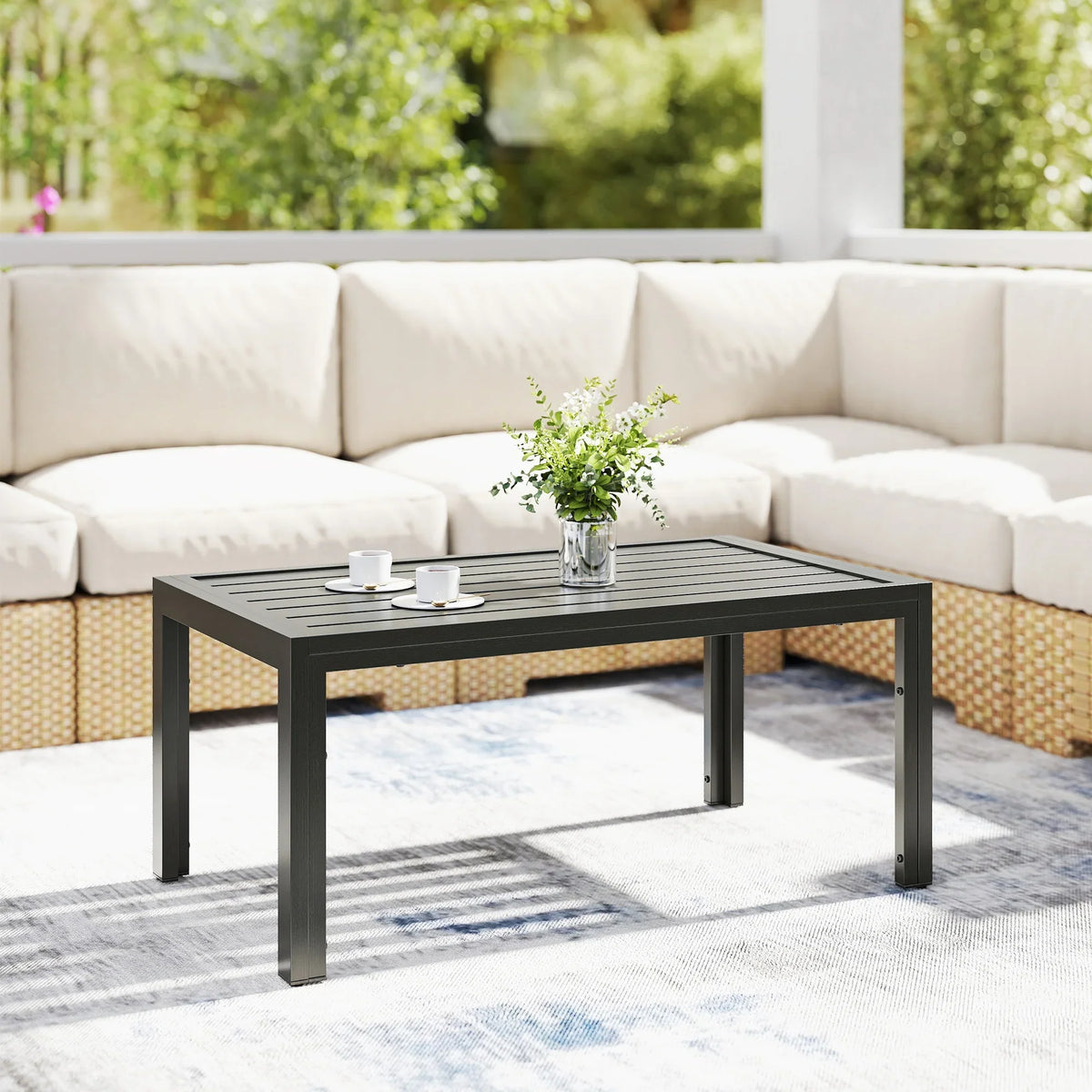 Grey outdoor rectangular side table with slatted top, placed between outdoor sofa cushions