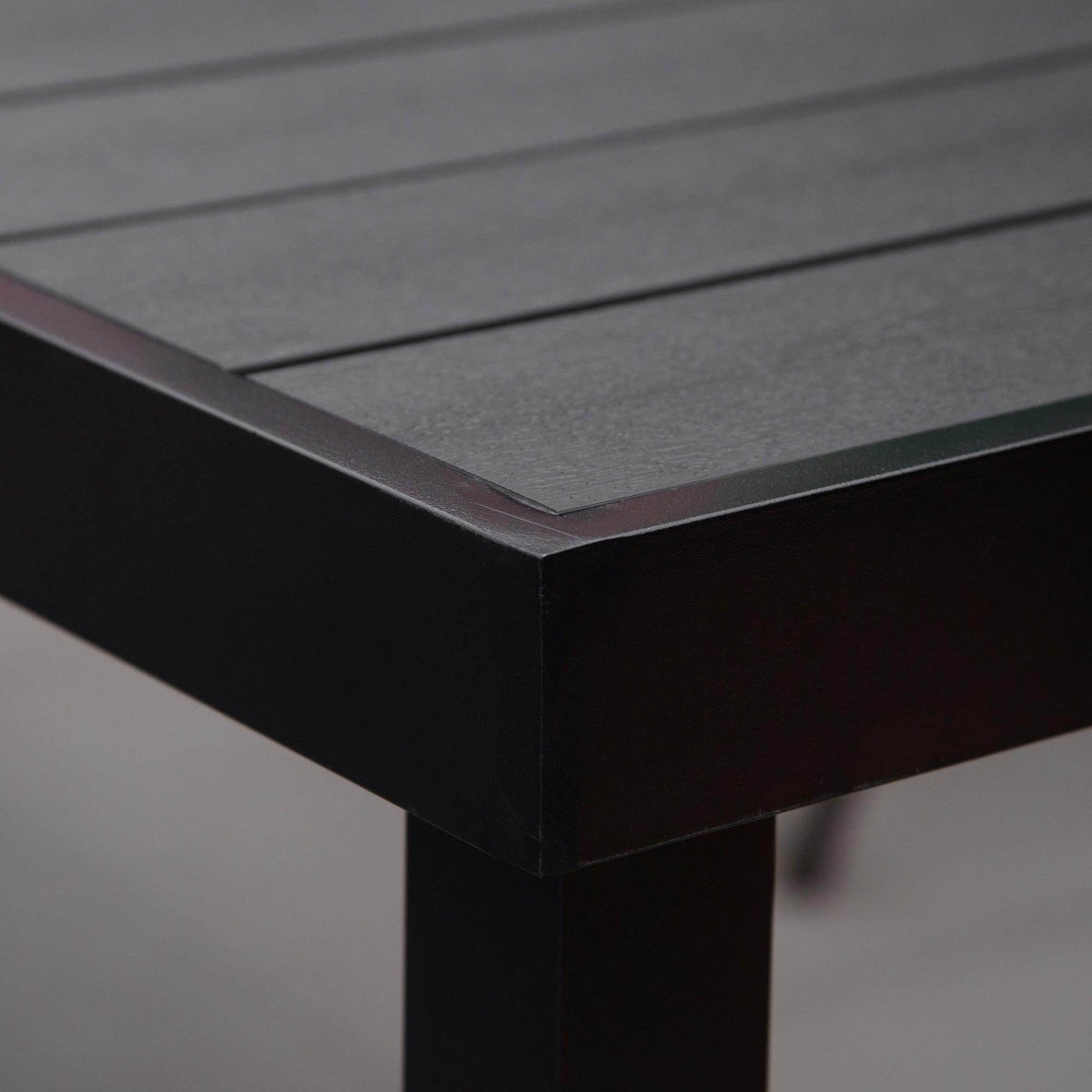 Black table corner with clean mitered edge and faux-wood effect surface.