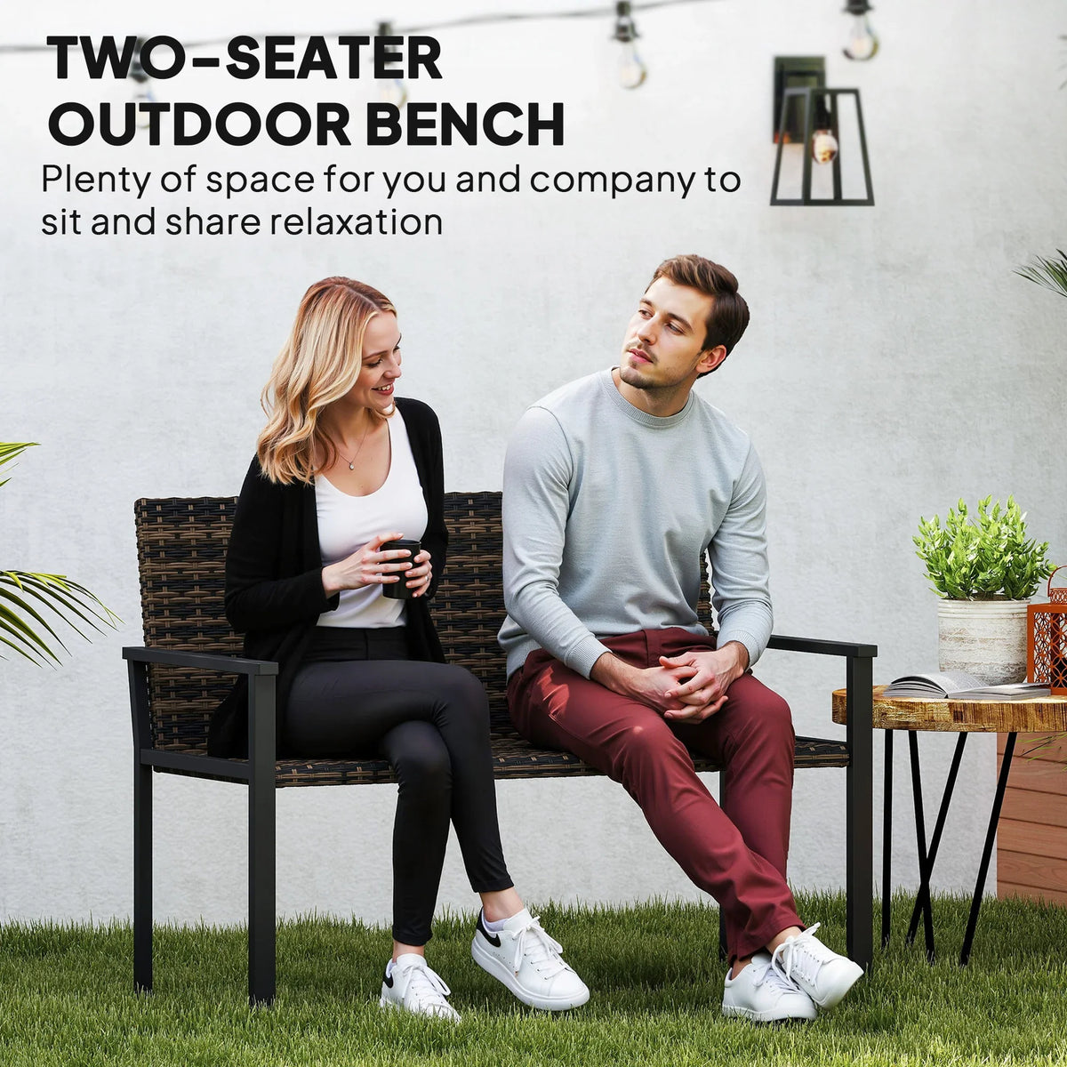 Two-seater outdoor rattan bench with two people seated, dark woven frame and armrests