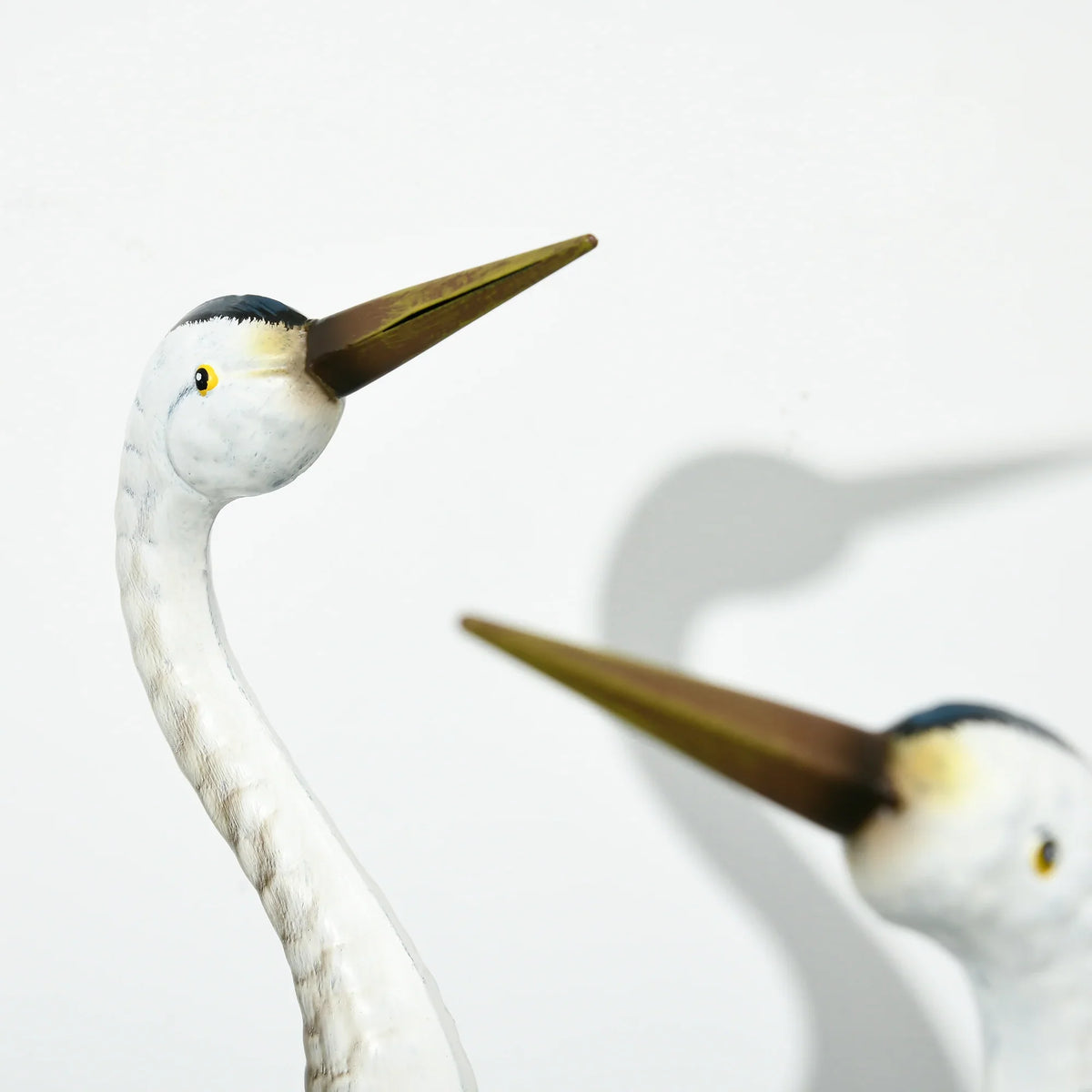 Close-up of two standing crane ornaments, white heads with yellow eyes and blue bodies
