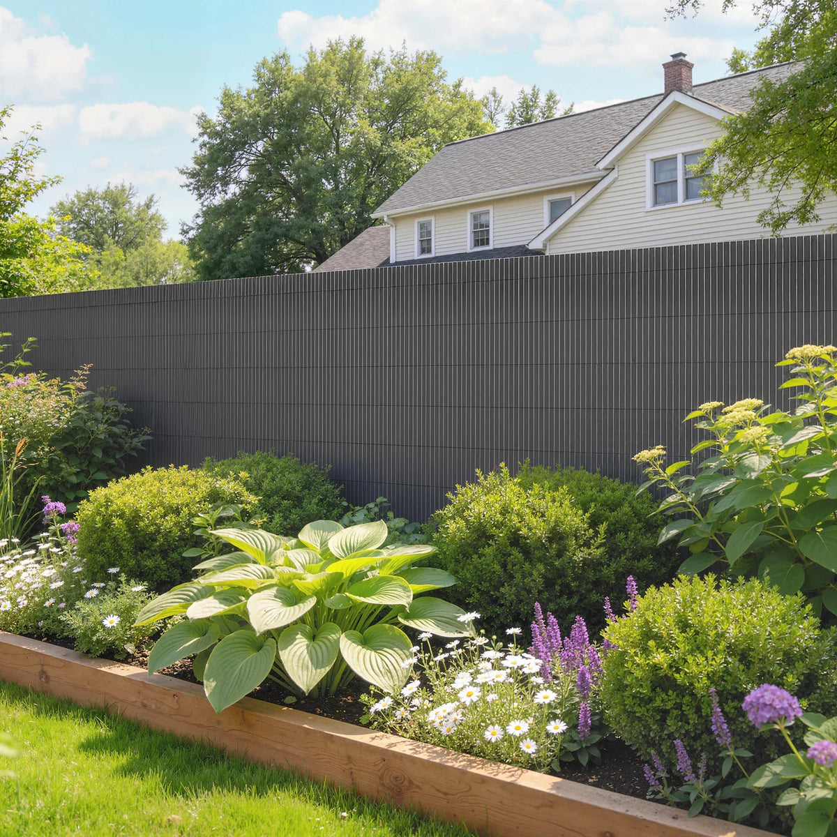 Dark grey plastic privacy fence along a flower garden bed and lawn.