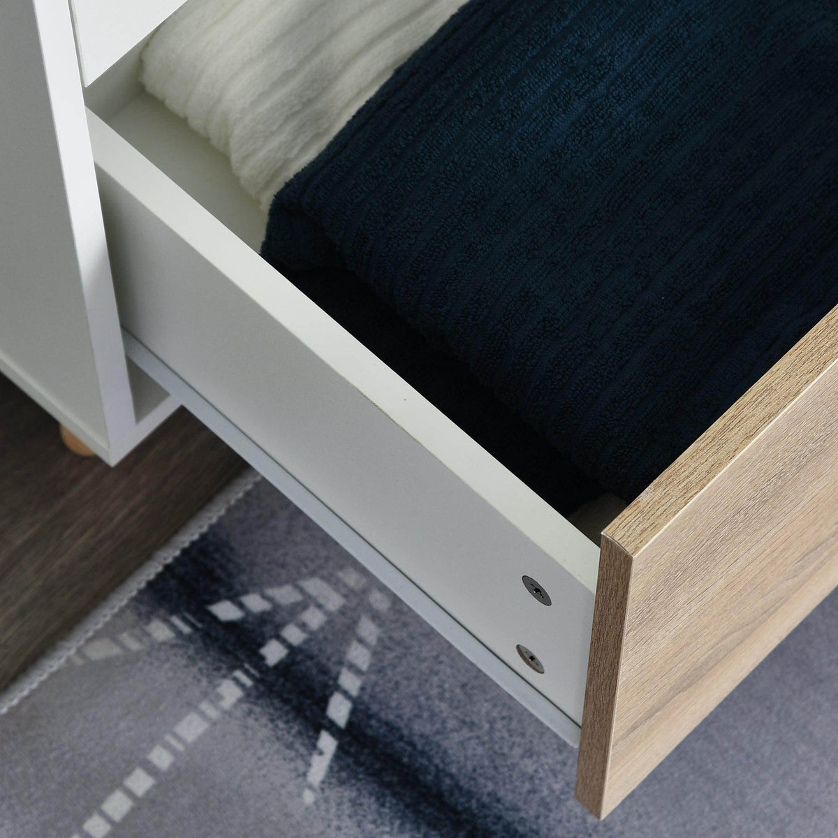 Lower drawer area with white frame and light wood front, holding folded dark bedding