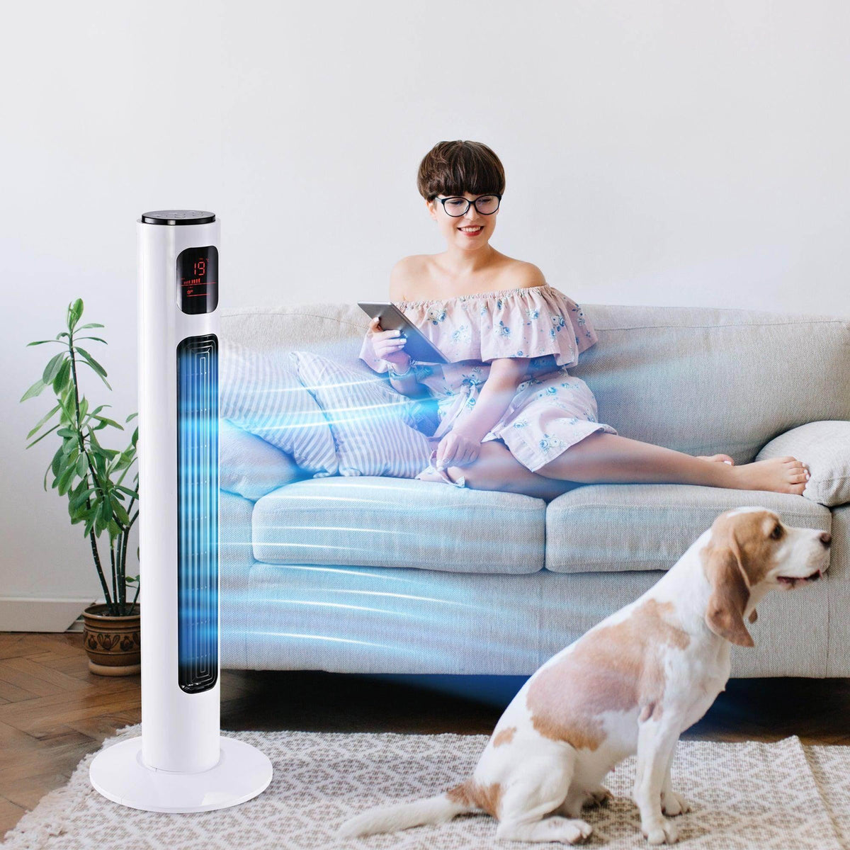 White tower fan on round base with glowing vertical air outlet beside couch