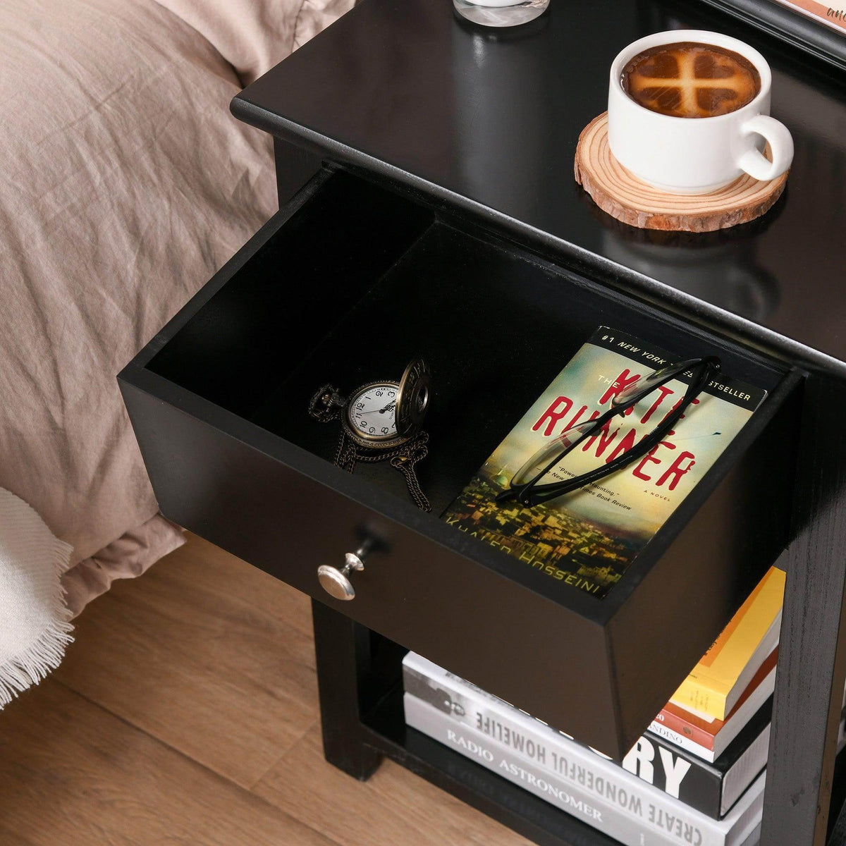 Black end table with open drawer and lower shelf holding books and decor