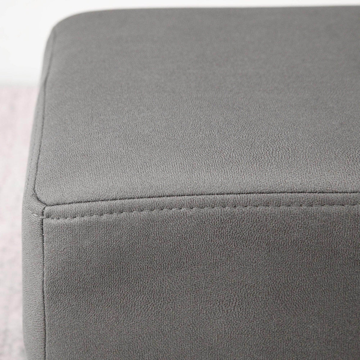 Grey upholstered foot rest ottoman corner with visible seam stitching