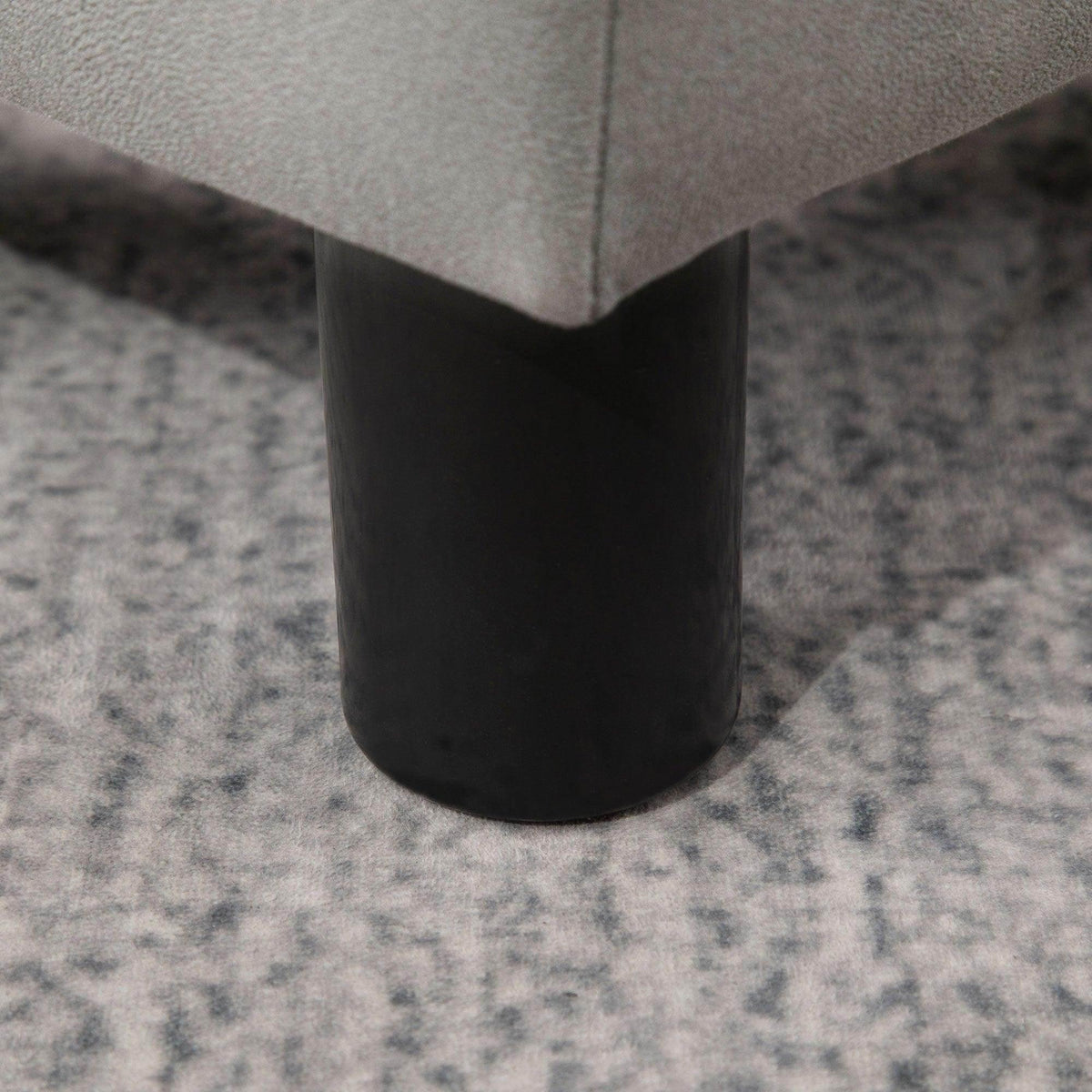 Black leg of grey foot rest ottoman with rounded base and corner view