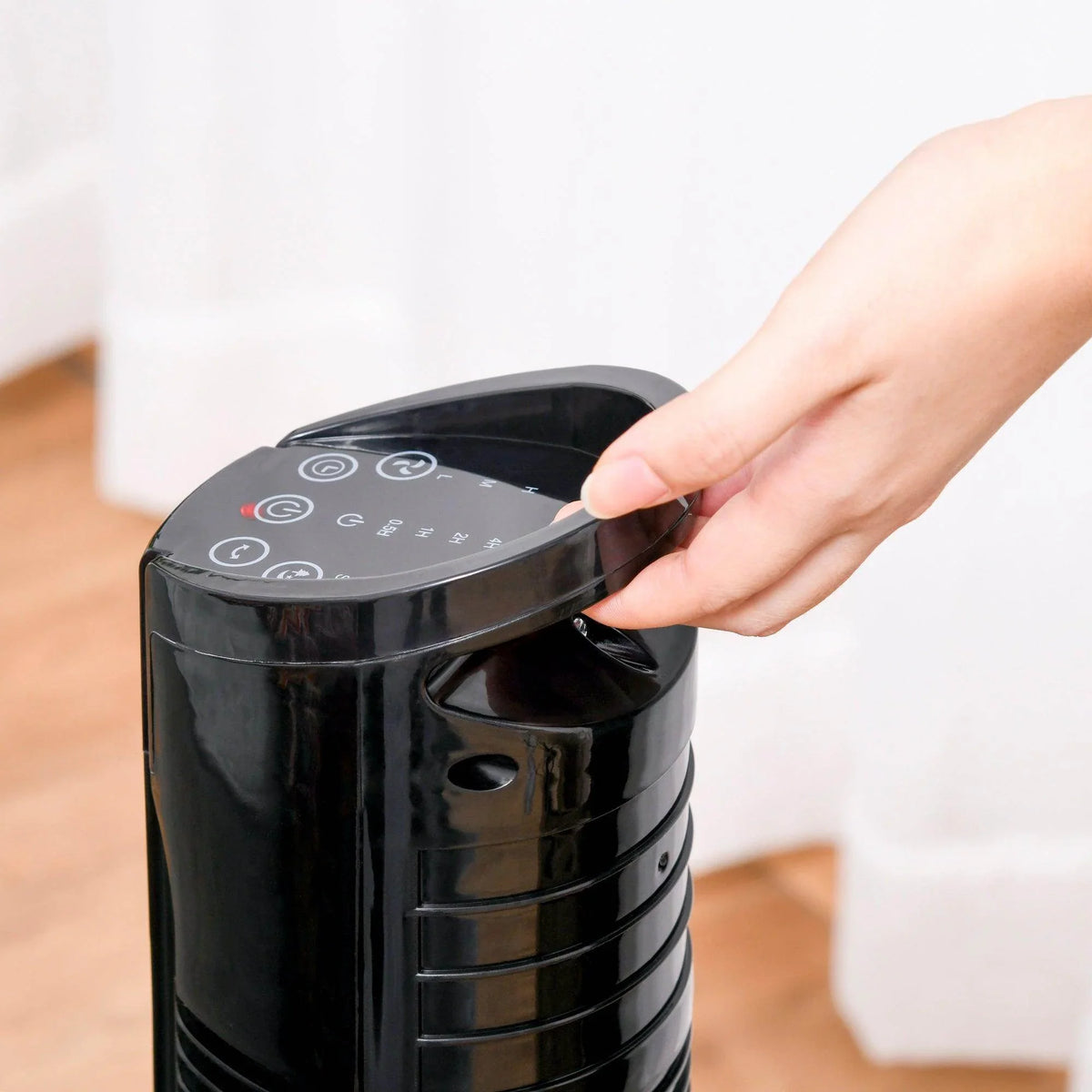 Black tower fan top control panel being pressed by a hand.