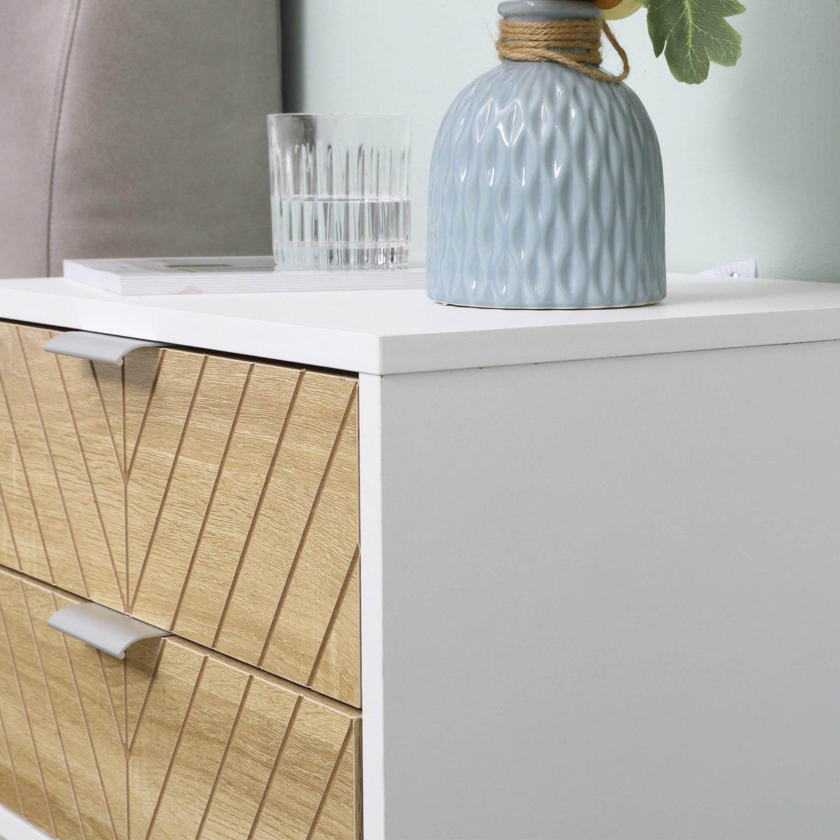 White bedside table close-up of drawer faces with gold-toned chevron pattern and pull handles