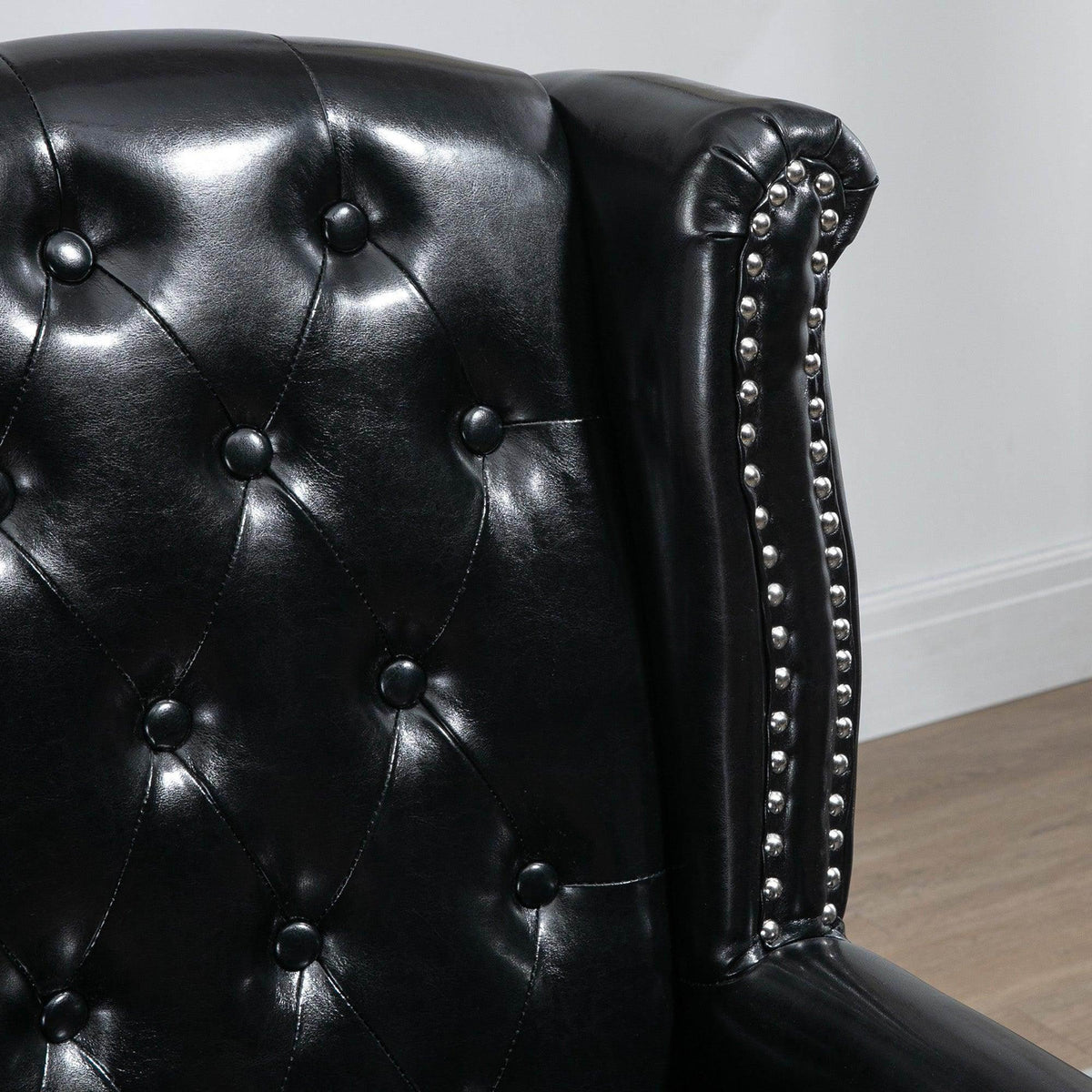 Close-up of black tufted wingback armchair backrest with studded nailhead trim