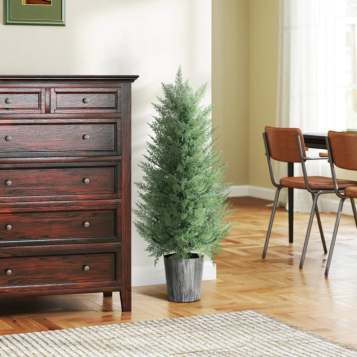 Artificial cypress tree in gray pot next to a wooden dresser and chairs