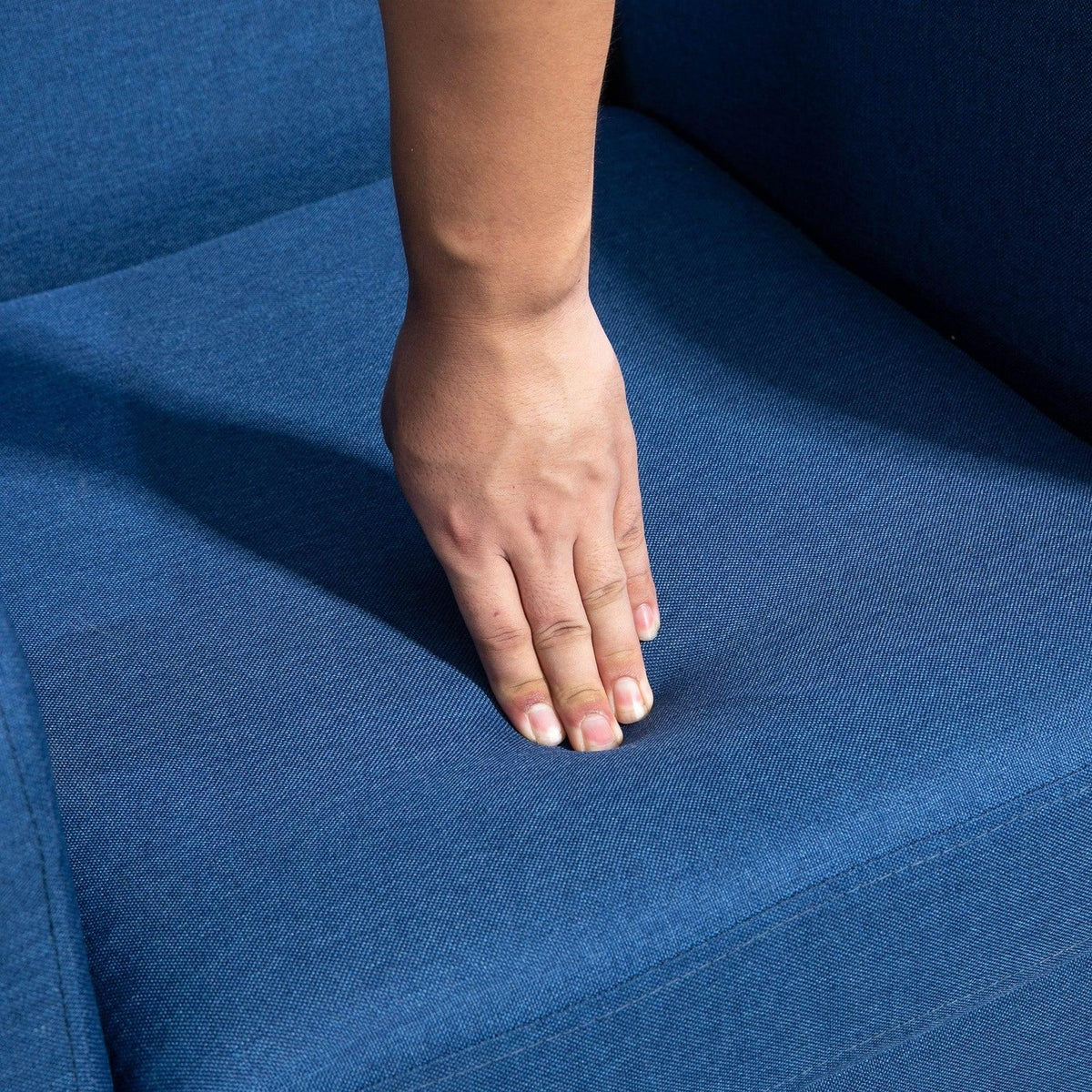 Blue accent chair seat cushion with a hand pressing to test comfort.