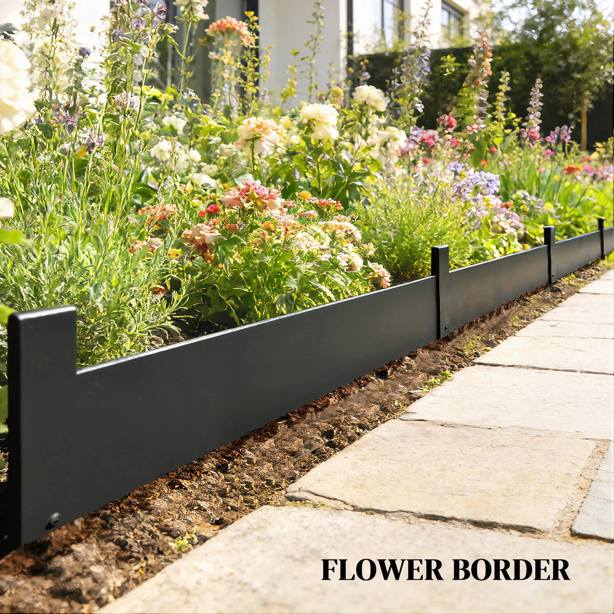 Black metal garden fence panel edging separating flower bed and stone walkway