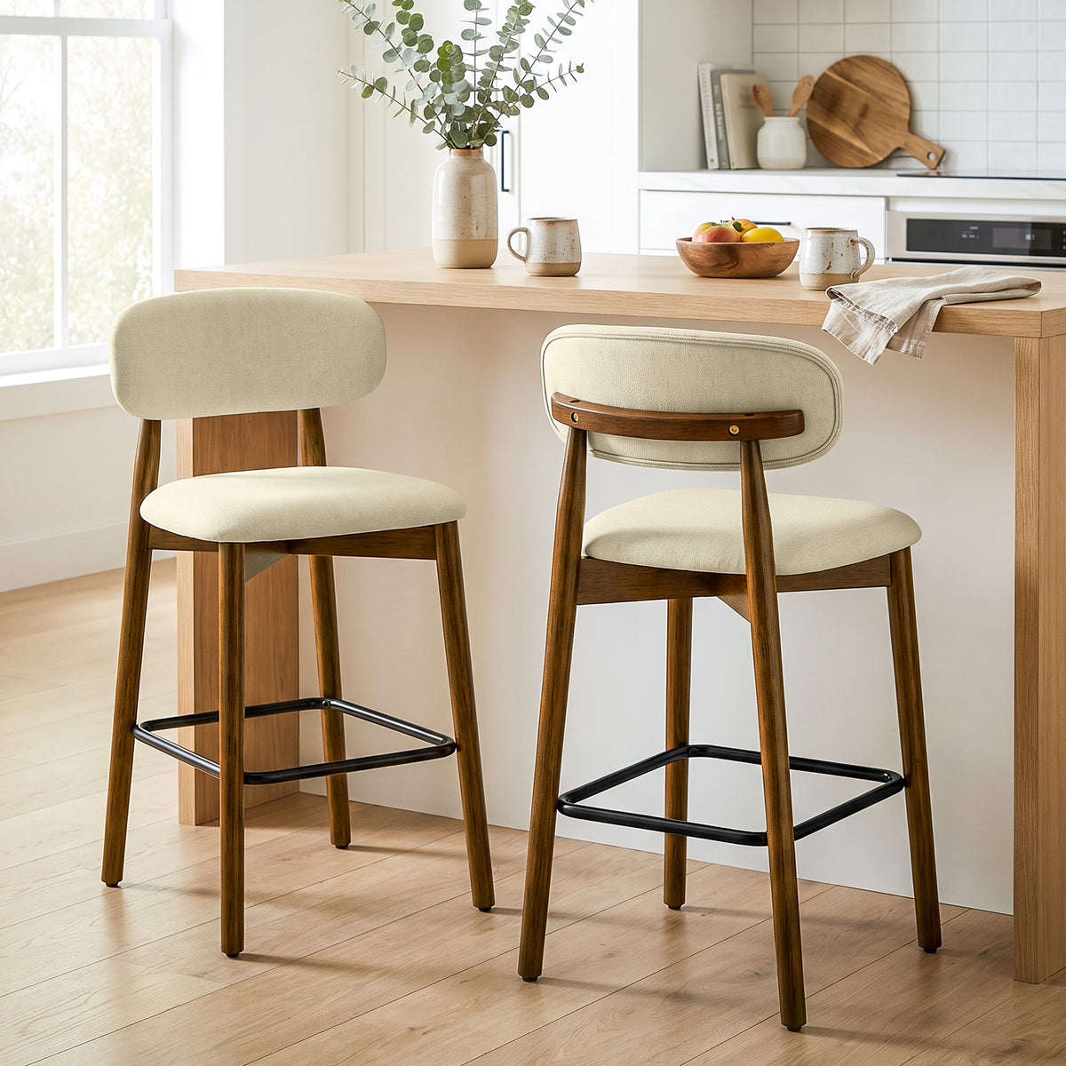 Set of 2 beige bar stools with cushioned seats, curved backs, black footrests