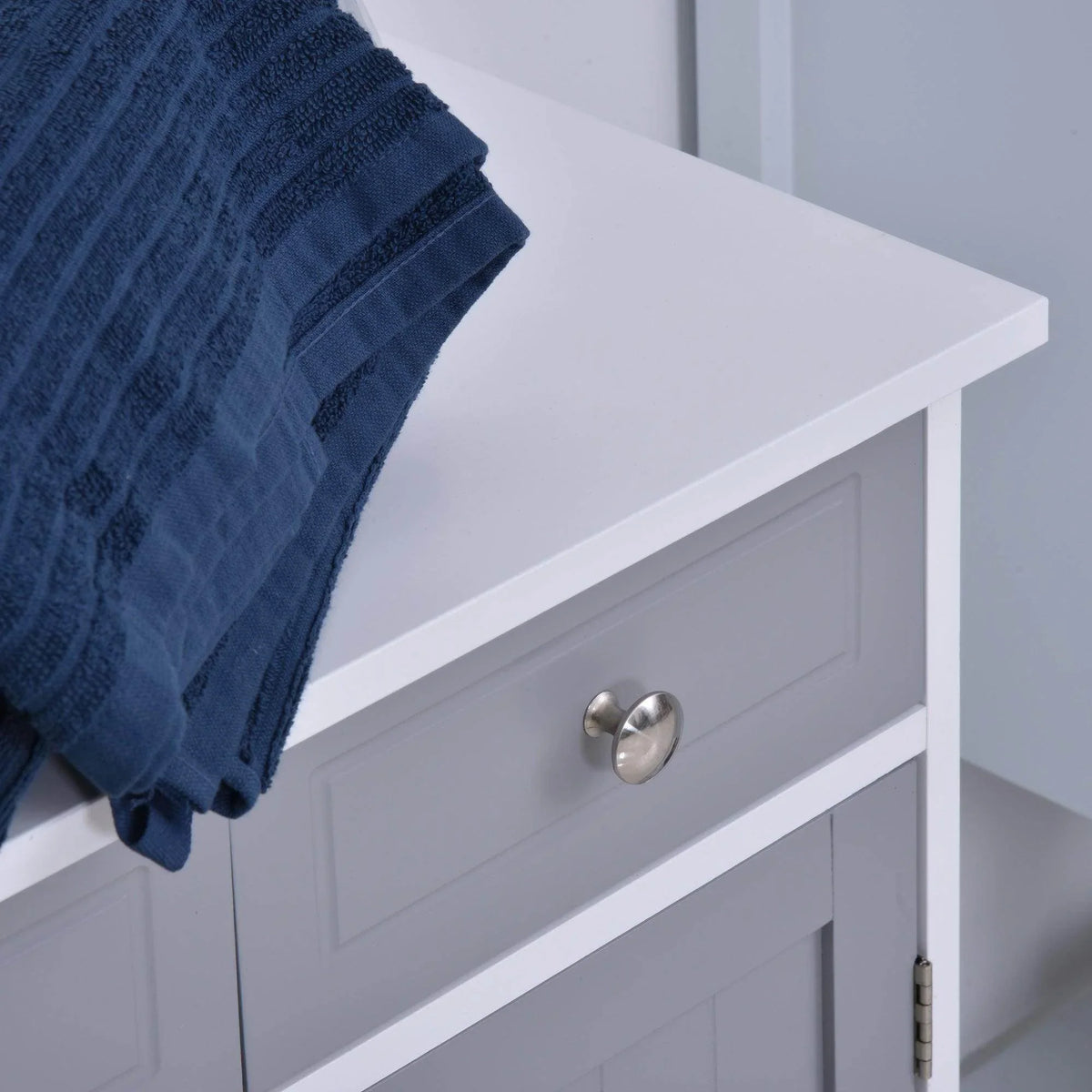 Grey bathroom cabinet drawer with round metal knob and part of the two-door base.