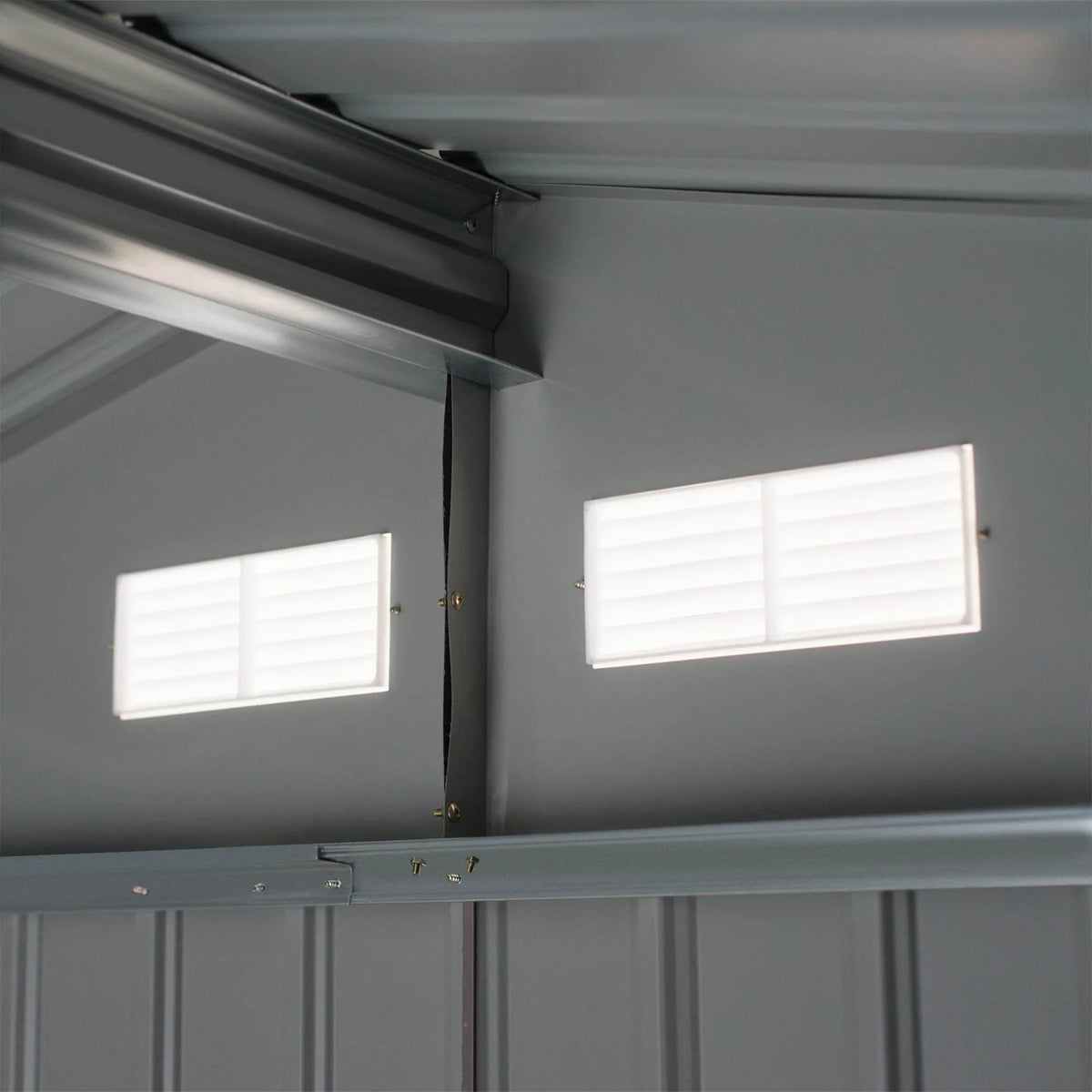 Grey shed interior with two louvered ventilation windows and upper roof supports.