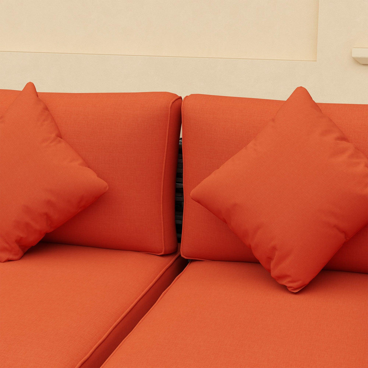Orange seat cushions with matching throw pillows on gray rattan sofa arms