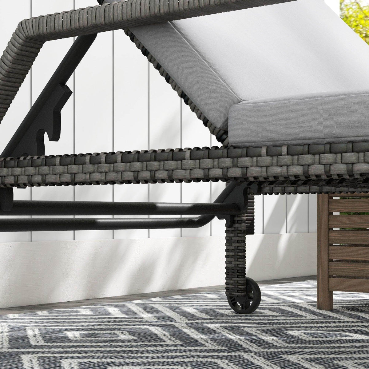Side view of dark rattan chaise lounger with cream-gray cushion and caster wheels