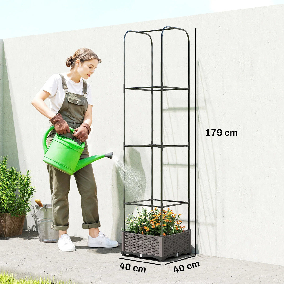 Gray plastic raised garden bed with tall trellis and flowers, shown beside a person