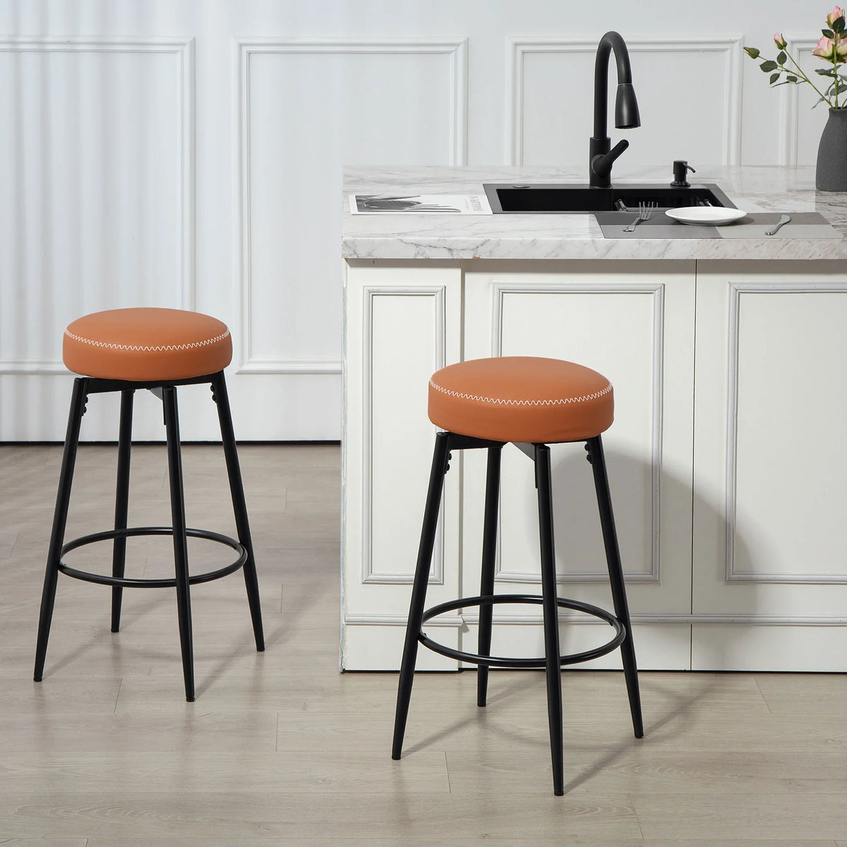 Set of two bar stools with round orange seats, white stitching, and black metal bases
