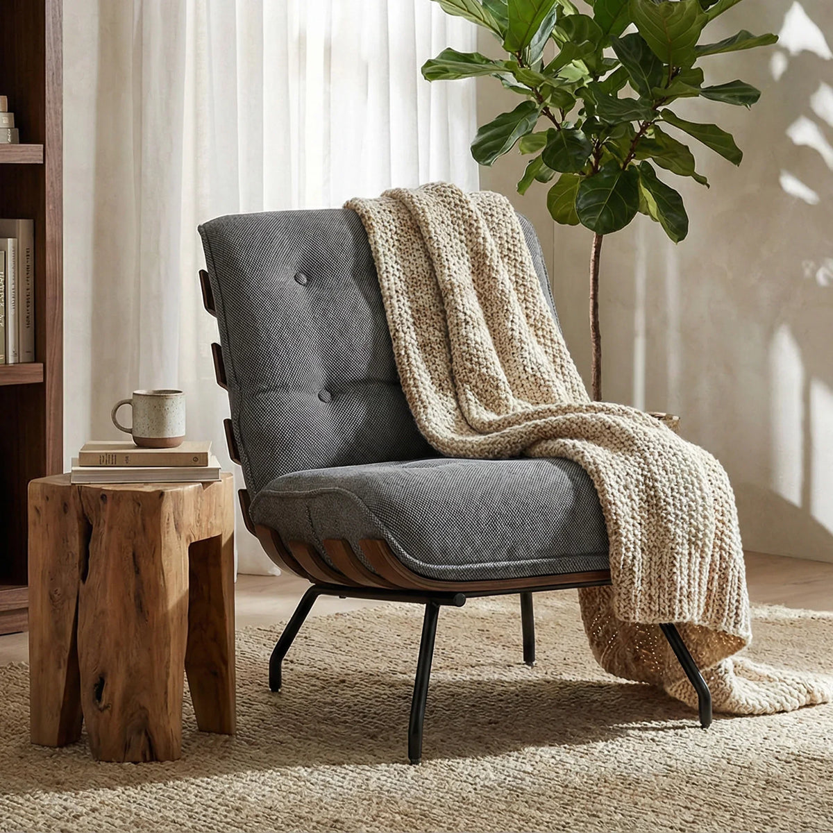 Dark grey accent reading chair with tufted backrest and curved arms, styled with a throw