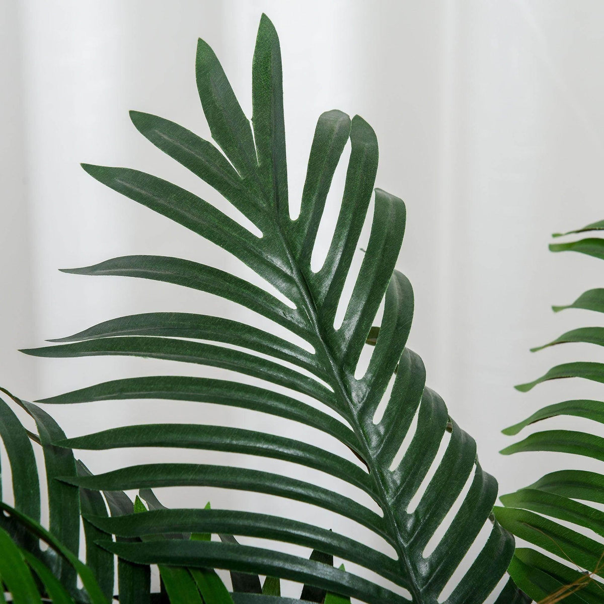 Artificial palm fronds detail in dark green with brown trunk base, black pot