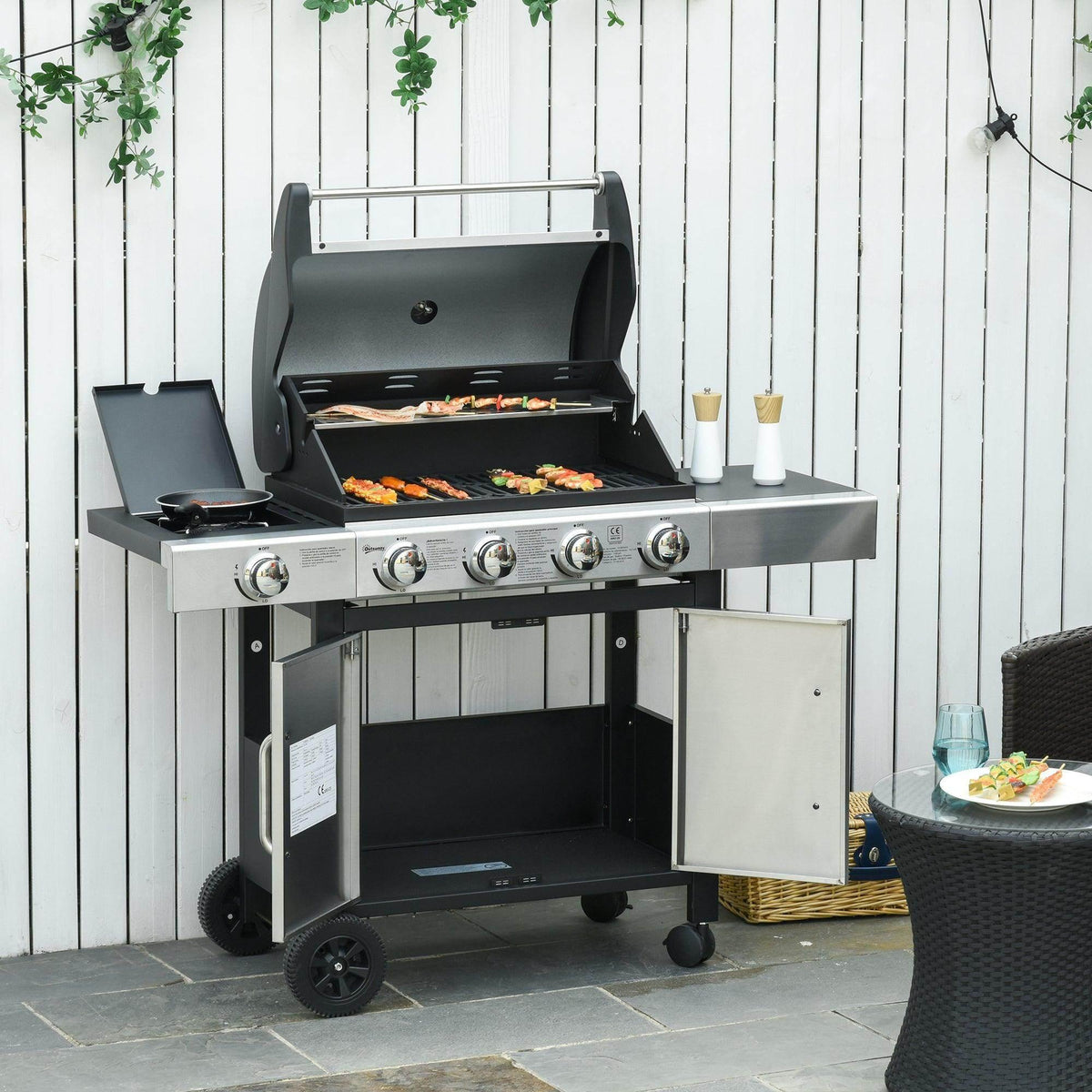 BBQ grill with lid open, stainless cart base, and food cooking on the grates