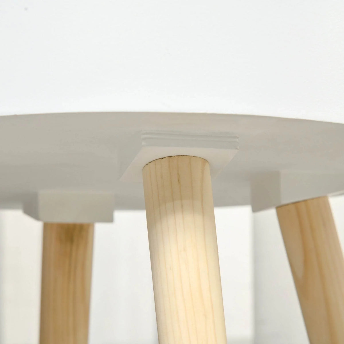 White round side table with light wood legs, underside close-up