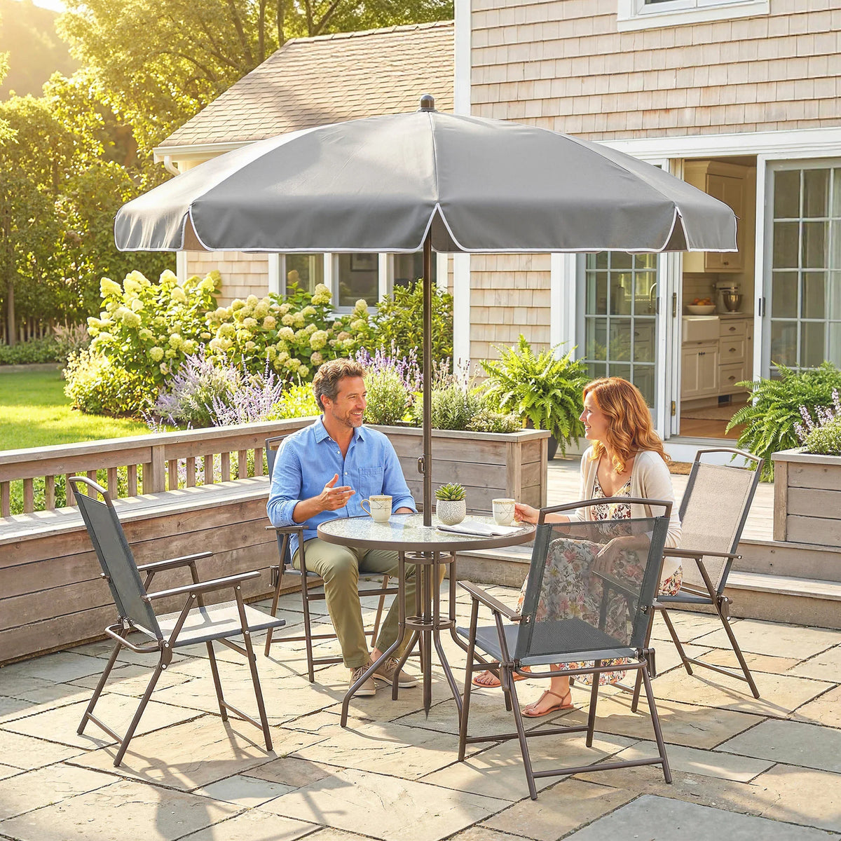 Outdoor patio dining set with open umbrella, round glass table, and 4 dark grey folding chairs