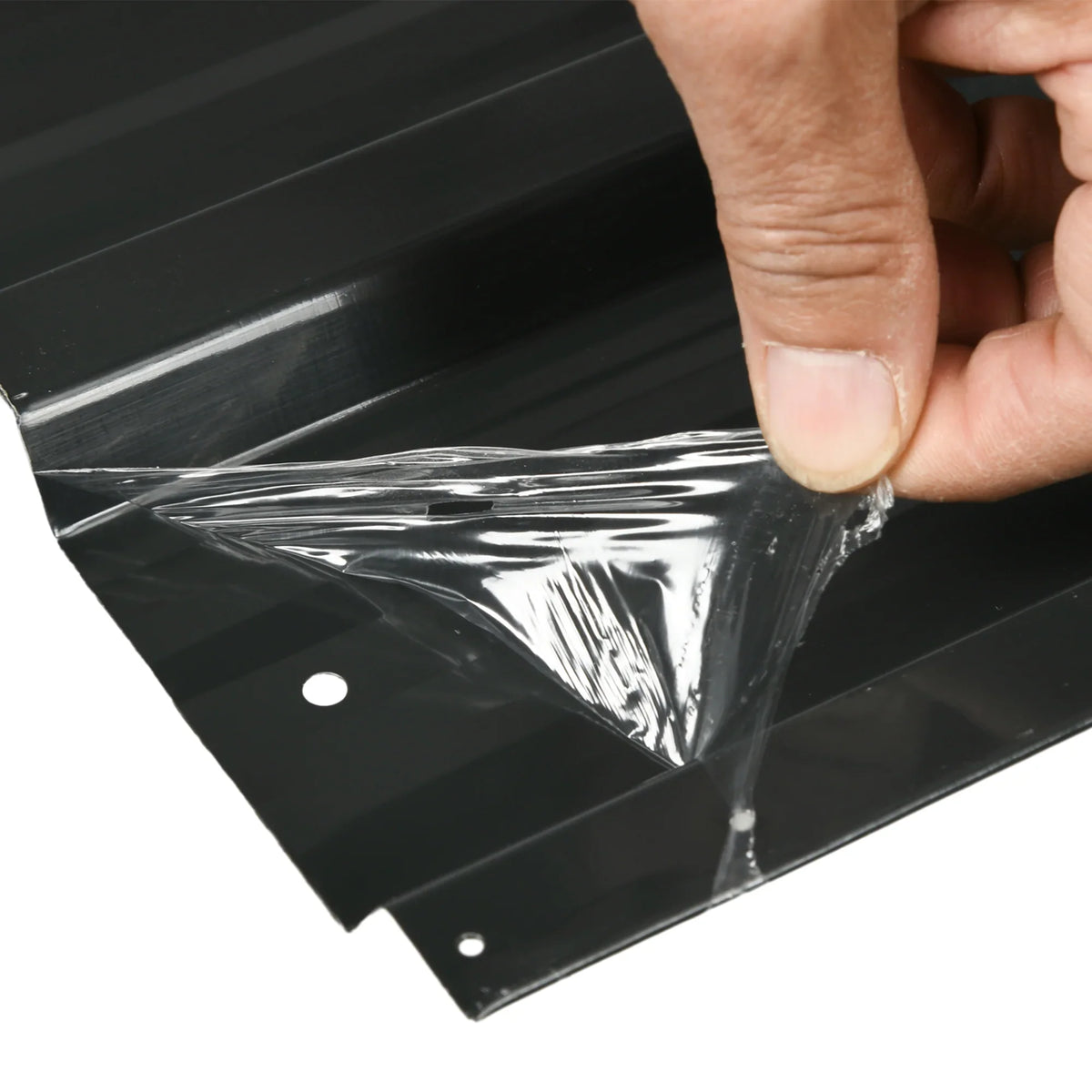 Hand peels protective film from dark grey corrugated roofing sheet with pre-made holes