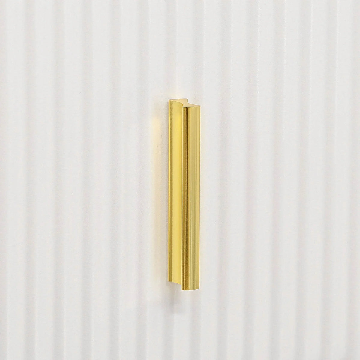 Gold vertical drawer handle on white ribbed cabinet front, close-up