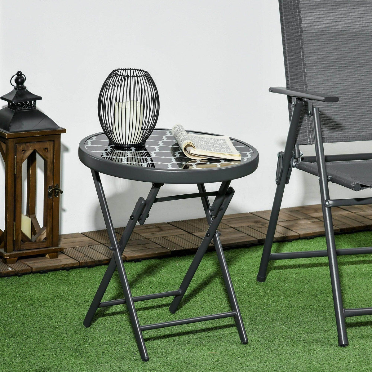 Black round folding patio side table with patterned glass top and tripod-style frame
