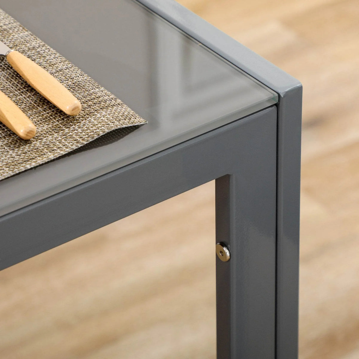 Grey metal table frame corner with smoky glass edge and securing hardware