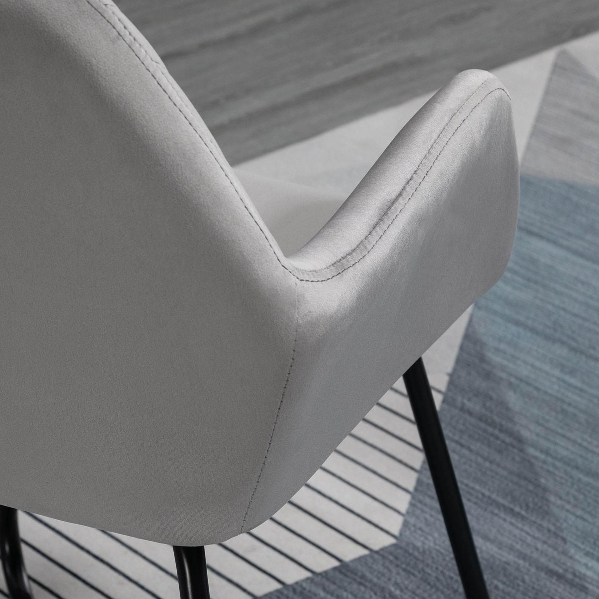 Grey upholstered armchair arm with curved stitching detail and black metal leg beneath.